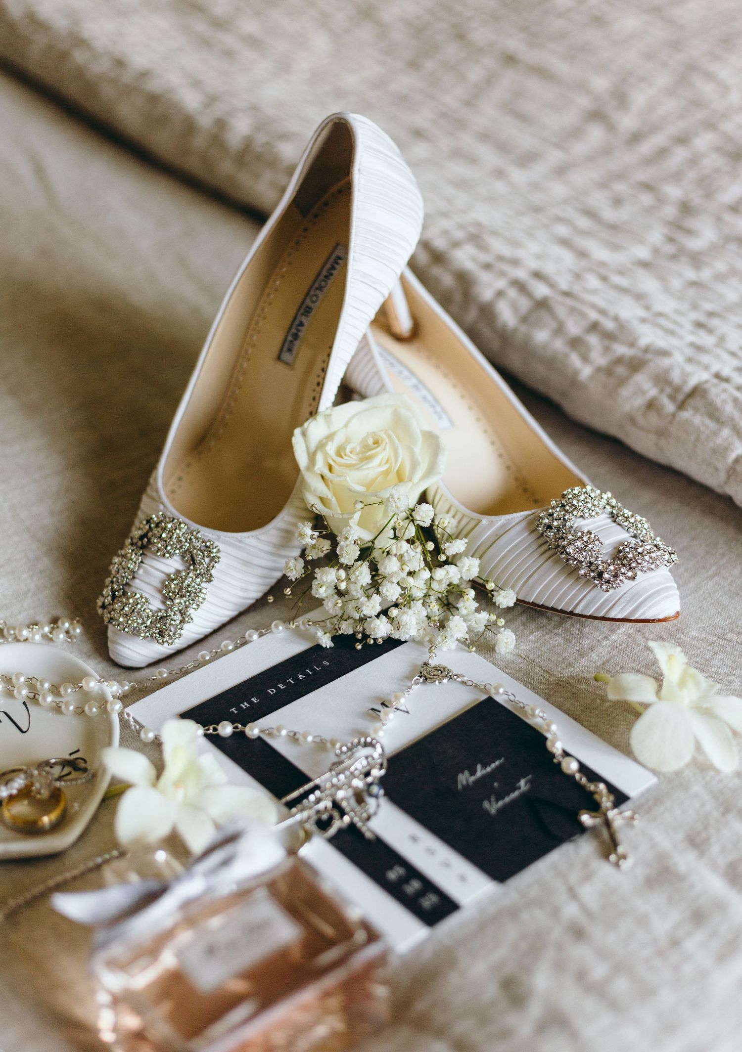 Wedding details featuring embellished white bridal shoes, invitations and delicate flowers.