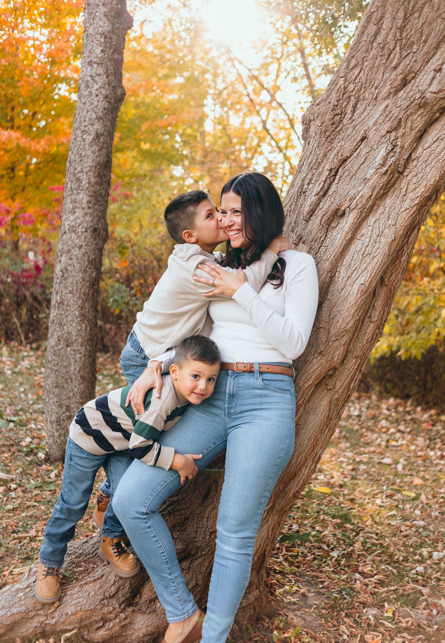 Autumn family photoshoot against large tree trunk with vibrant orange fall foliage.