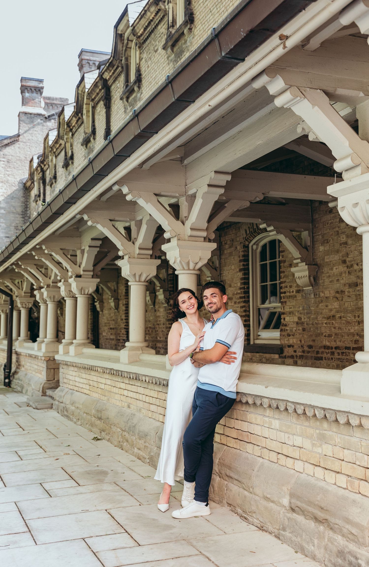 A couple poses beneath ornate white pillars of a historic Gothic-style building.