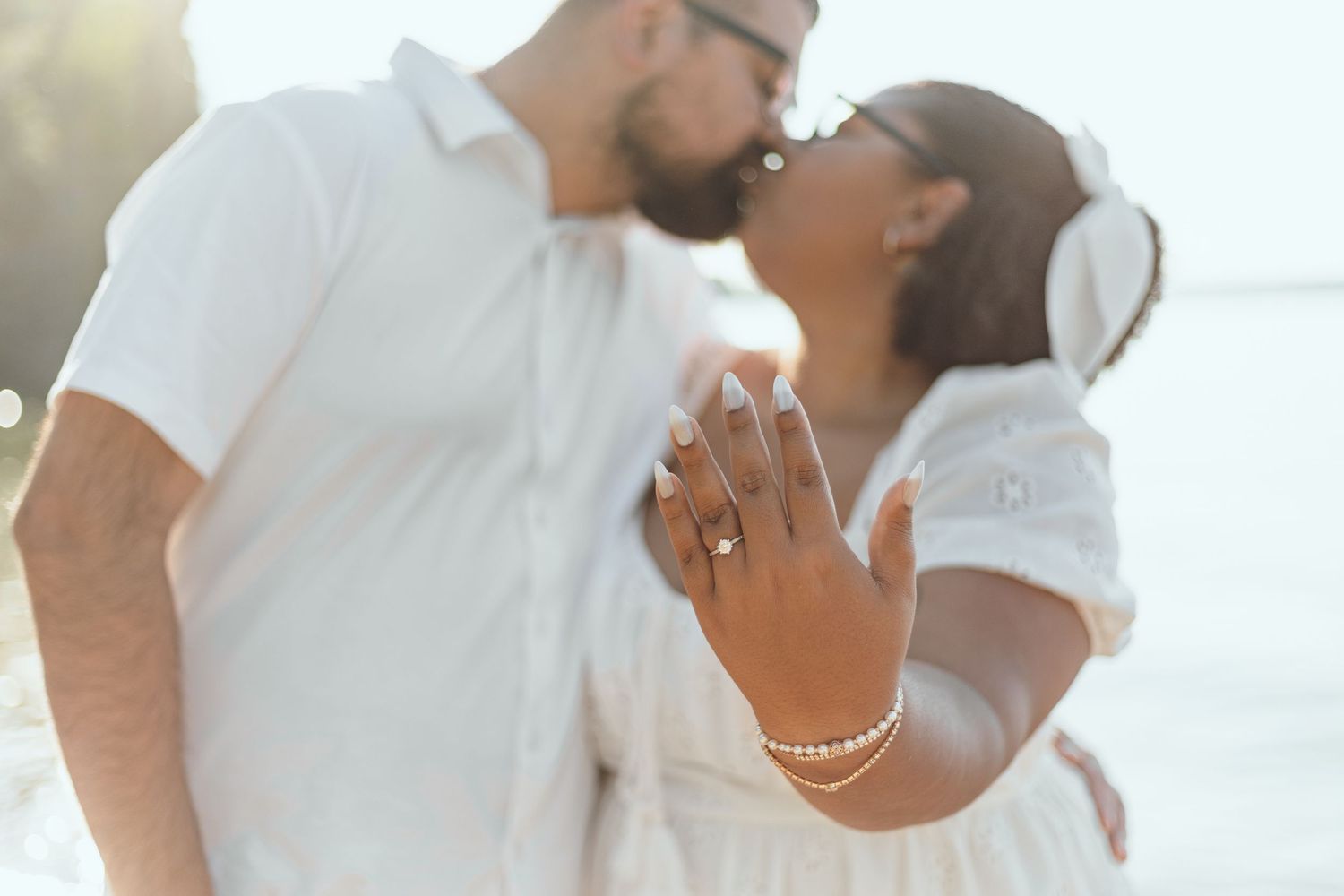 A couple in white outfits embraces against a bright sunlit background.