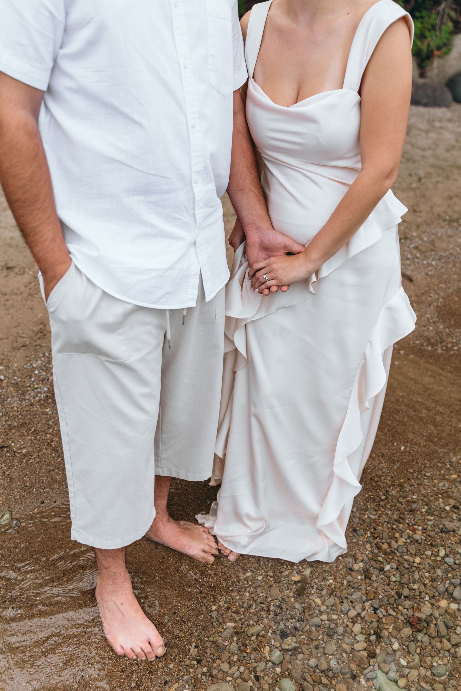 Couple wearing all white clothing photographed from waist down standing on rocky ground.