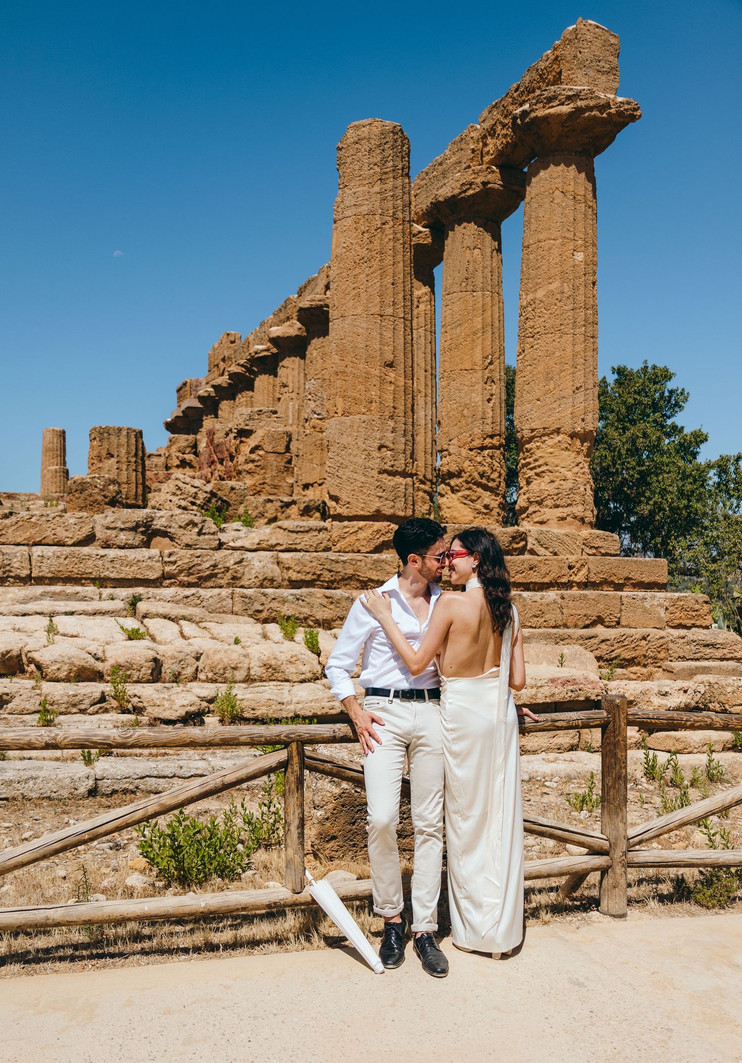 Couple in matching white outfits share intimate moments among historic temple ruins in Sicily.
