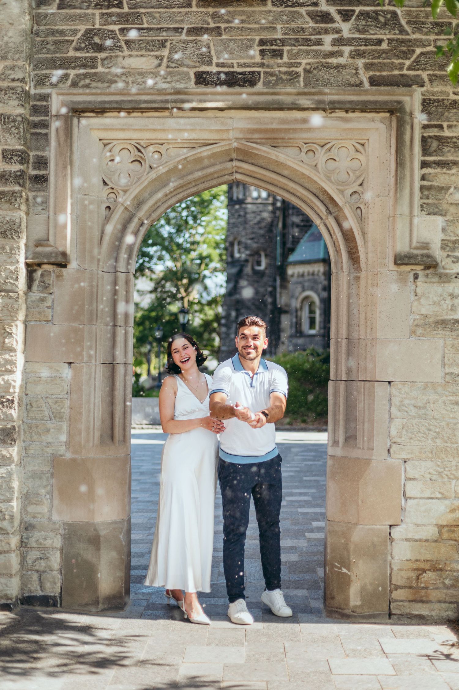 A couple laughs together while standing in an ornate stone archway.