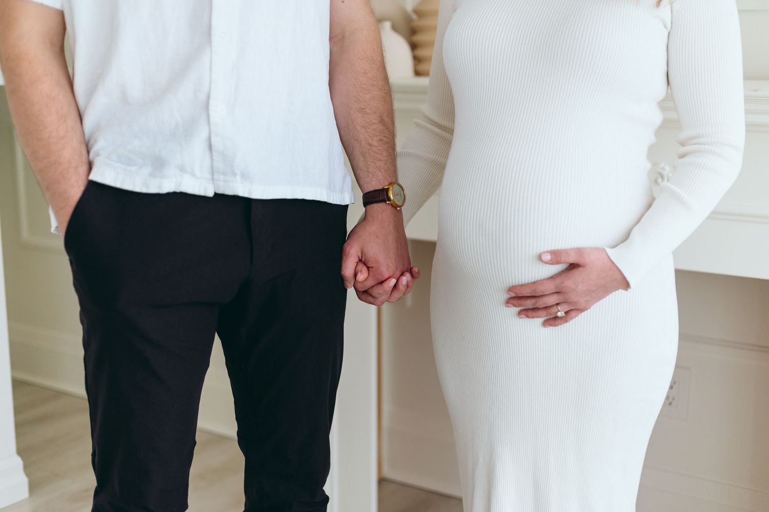 Intimate maternity photoshoot featuring couple in white against bright background.