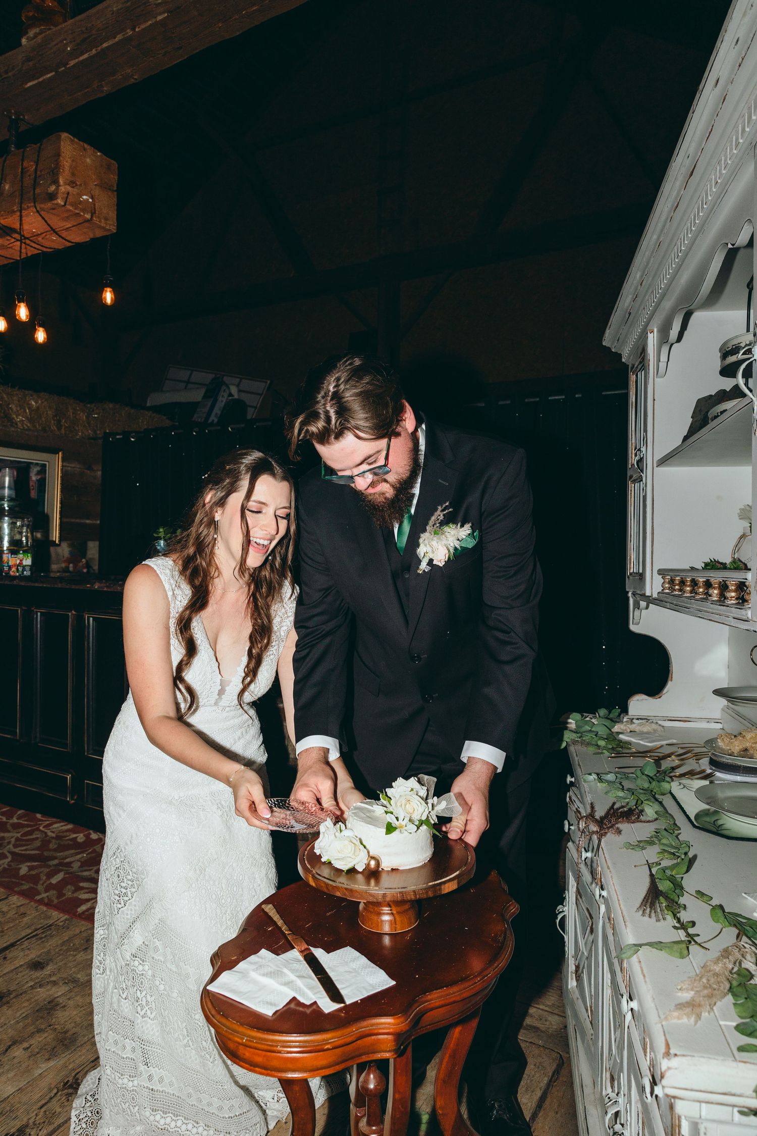 Newlyweds sharing cake cutting moment at rustic reception venue.