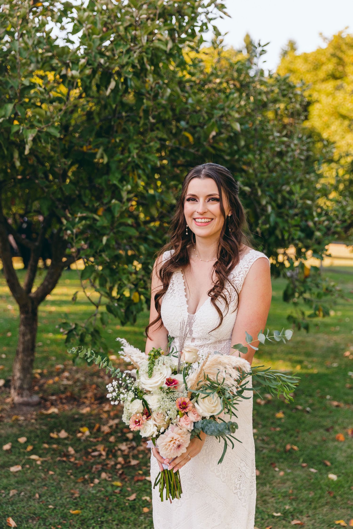 A wedding portrait in an orchard with soft autumn lighting and a blush floral bouquet.