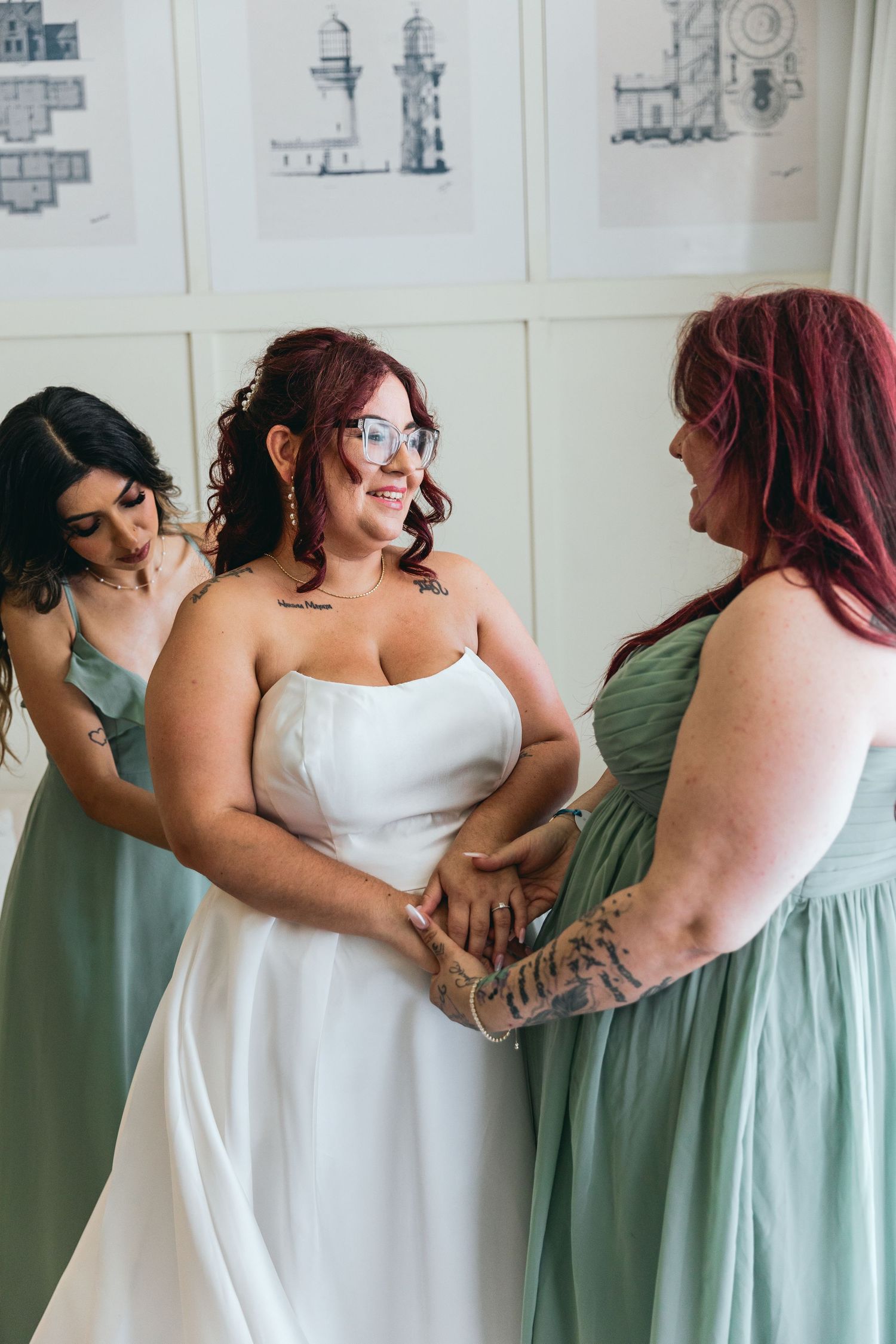 Wedding party members in sage green dresses and white gowns embrace while showing off their coordinated outfits.