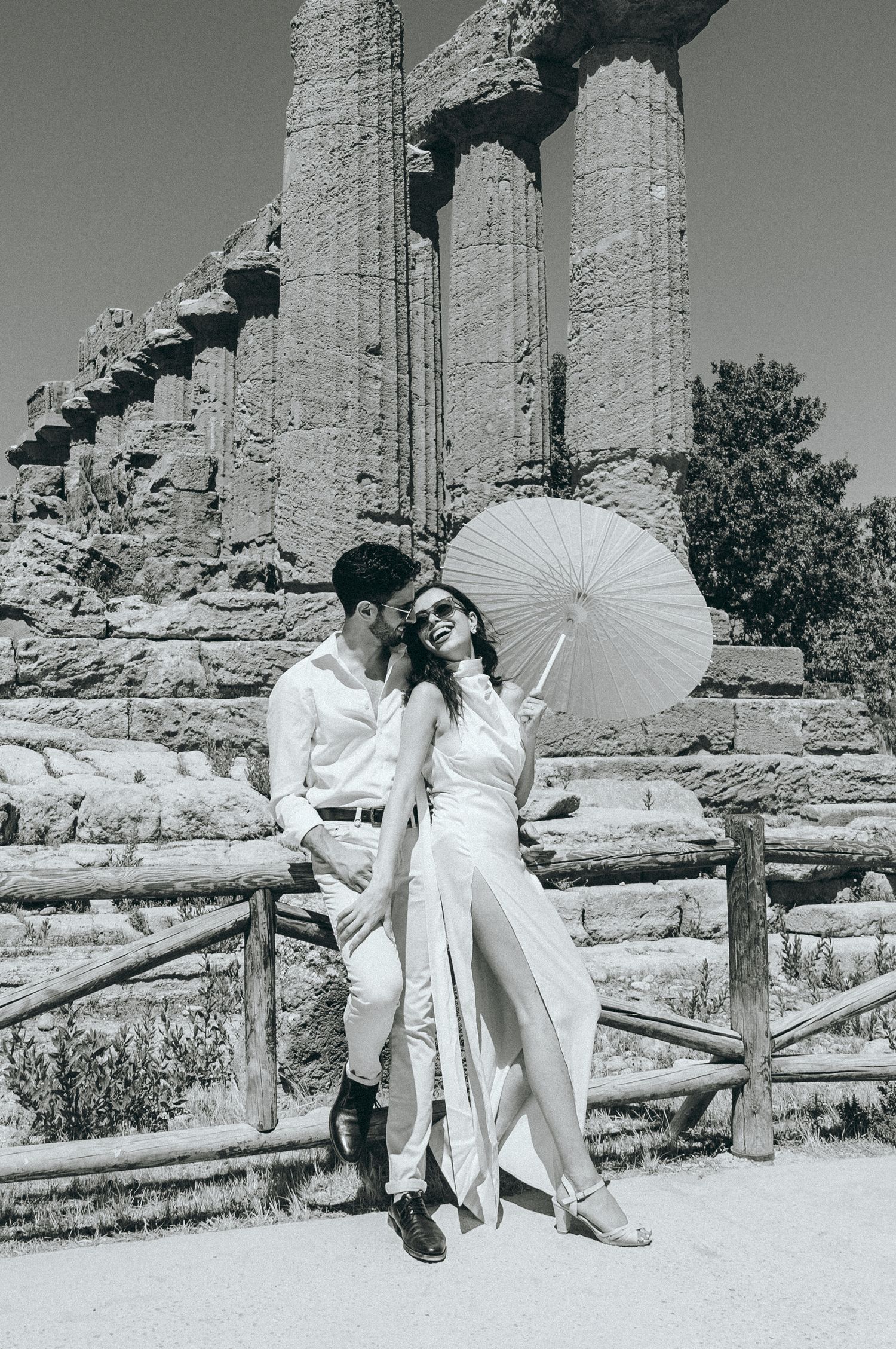 Elegant photo shoot with white parasol against backdrop of ancient stone columns.