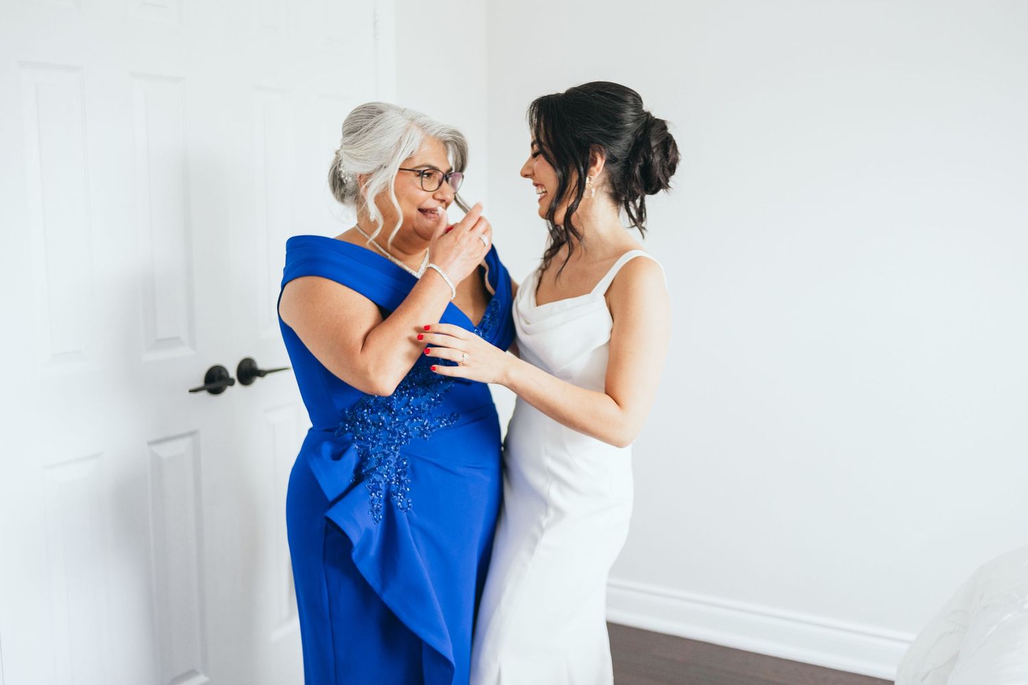 Two people share an emotional moment in formal attire, one wearing a royal blue dress and one in white.