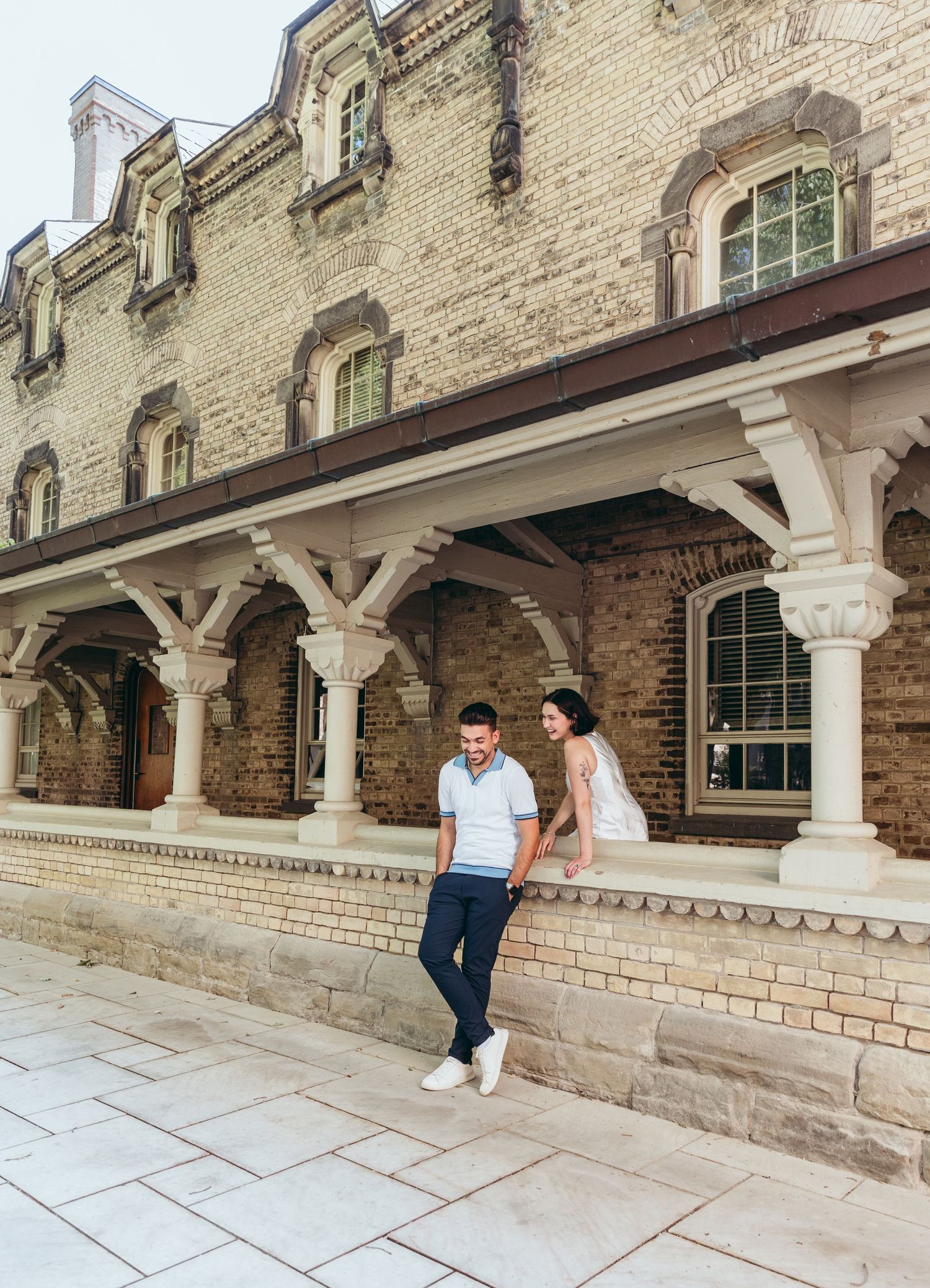 A couple poses against a historic brick building with ornate white columns.