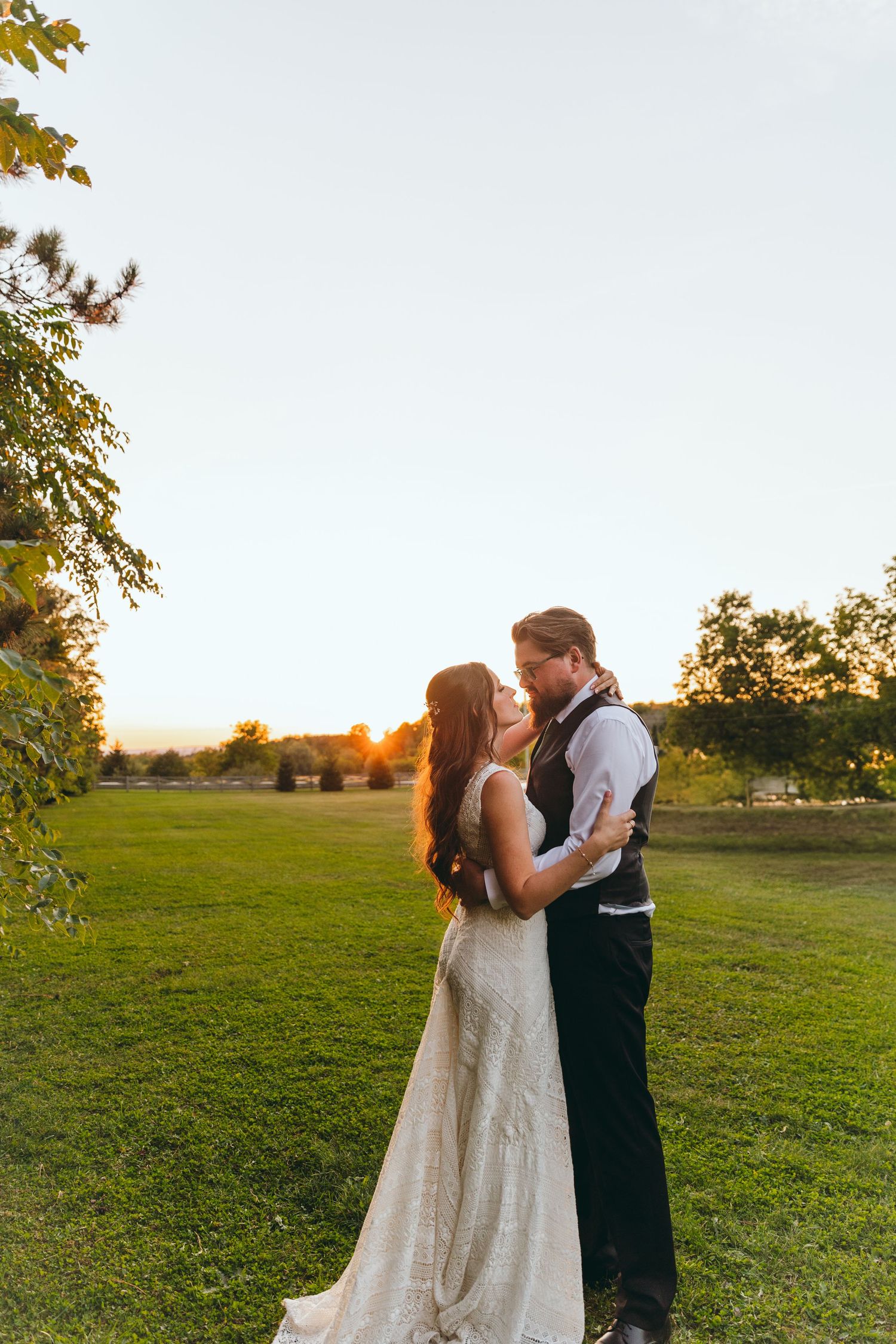 Couple shares intimate moment during golden hour in an open field at sunset.