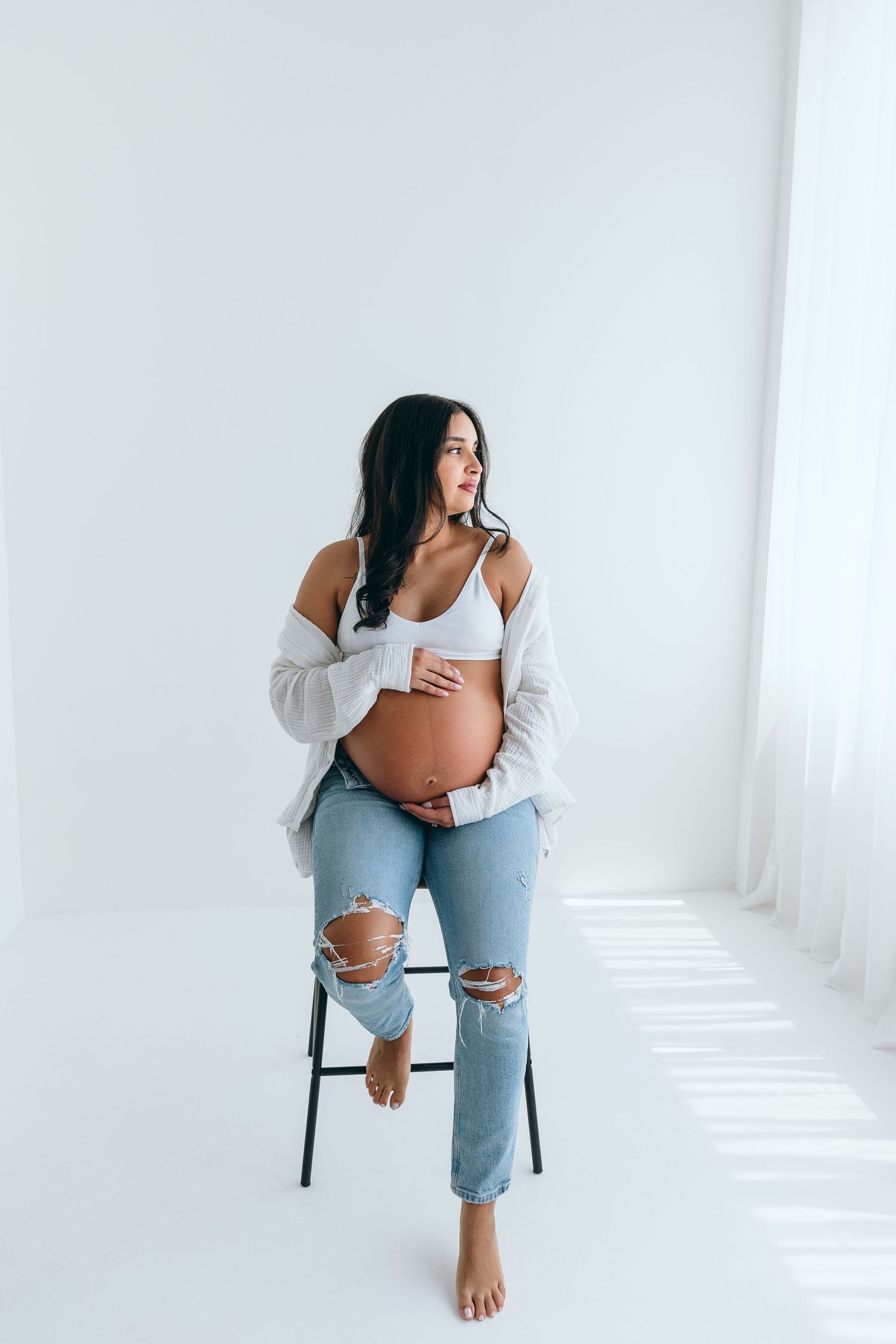 Side view of expectant mother in relaxed pose on chair against white wall.