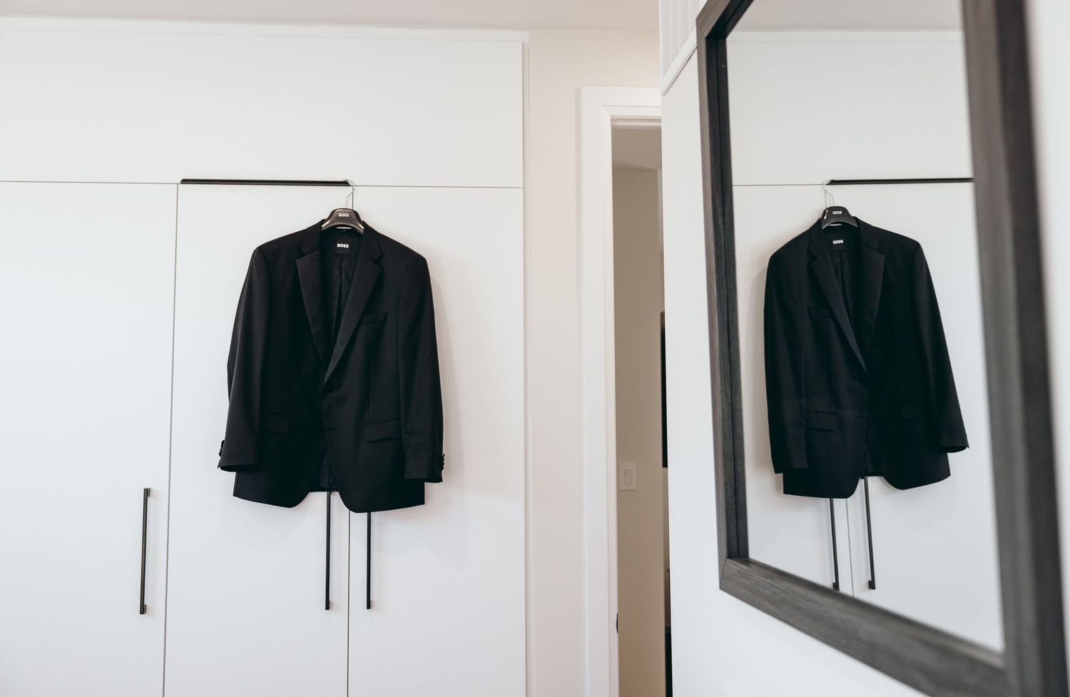 A black tuxedo jacket hanging on a white closet door with a mirror reflection.
