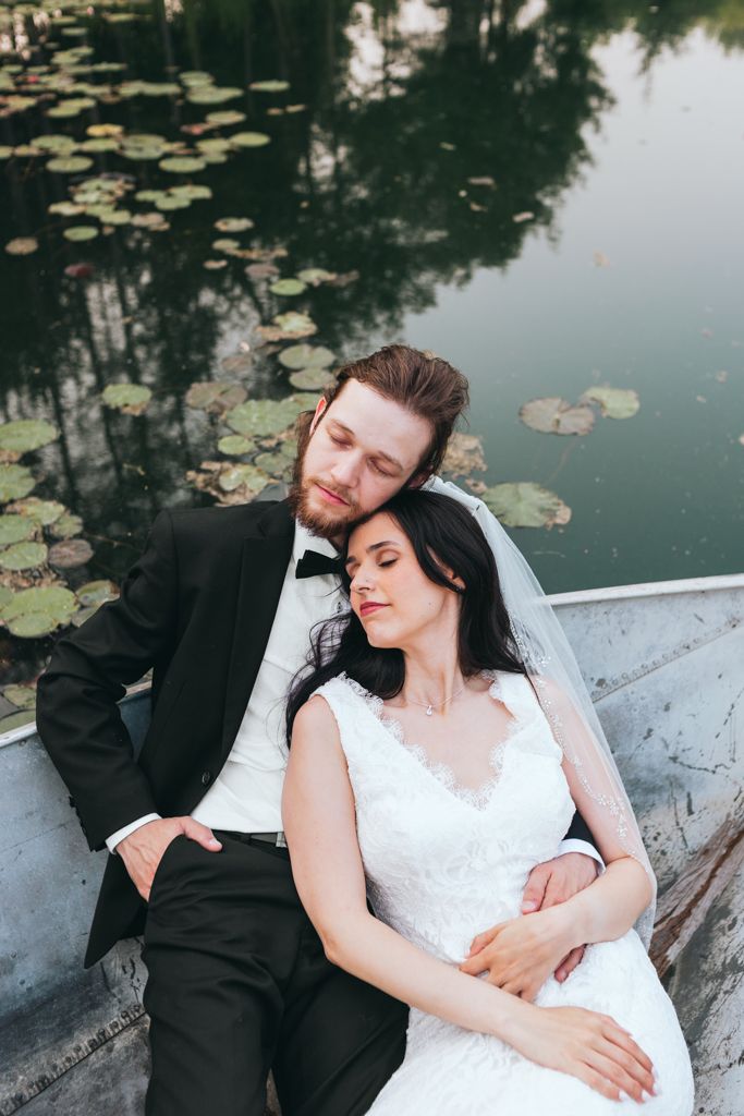 Newlyweds share an intimate moment while resting in a rowboat near water lilies.