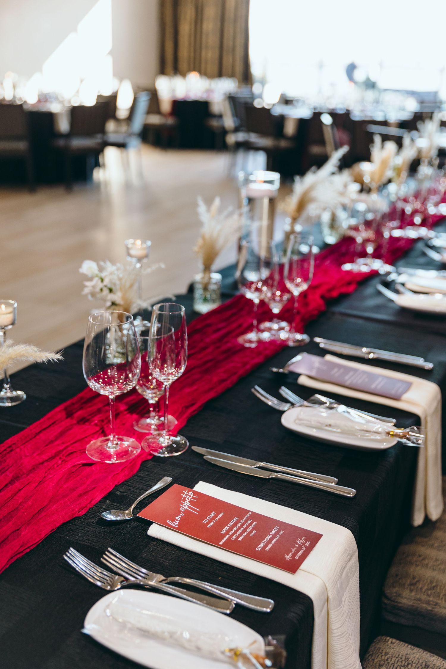 Elegant wedding reception table settings with black tablecloths, red runners, and crystal wine glasses.