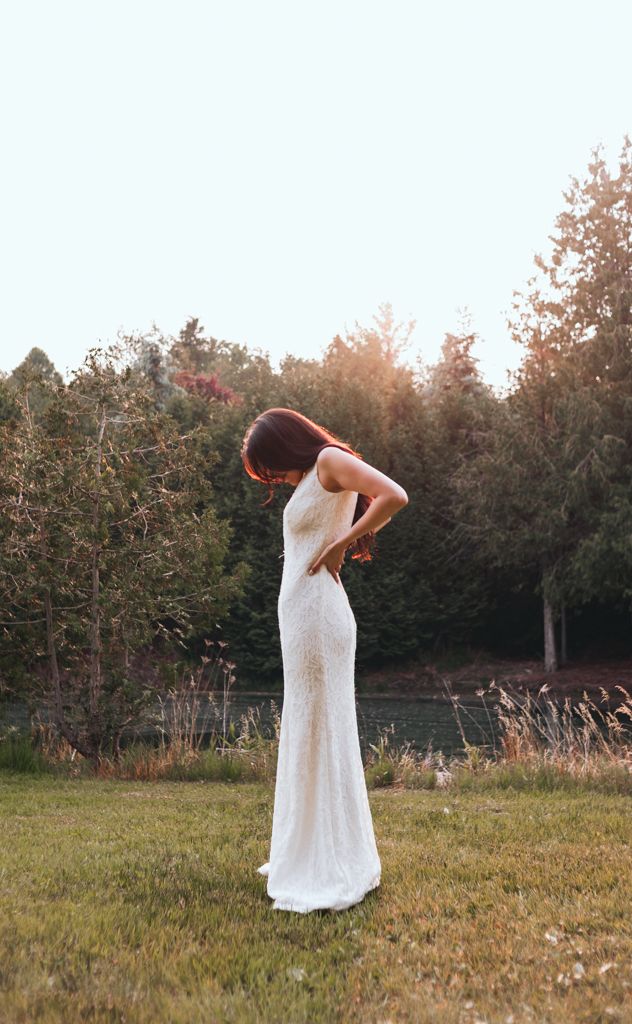 Bride in white lace dress poses gracefully in a sunlit meadow at golden hour.