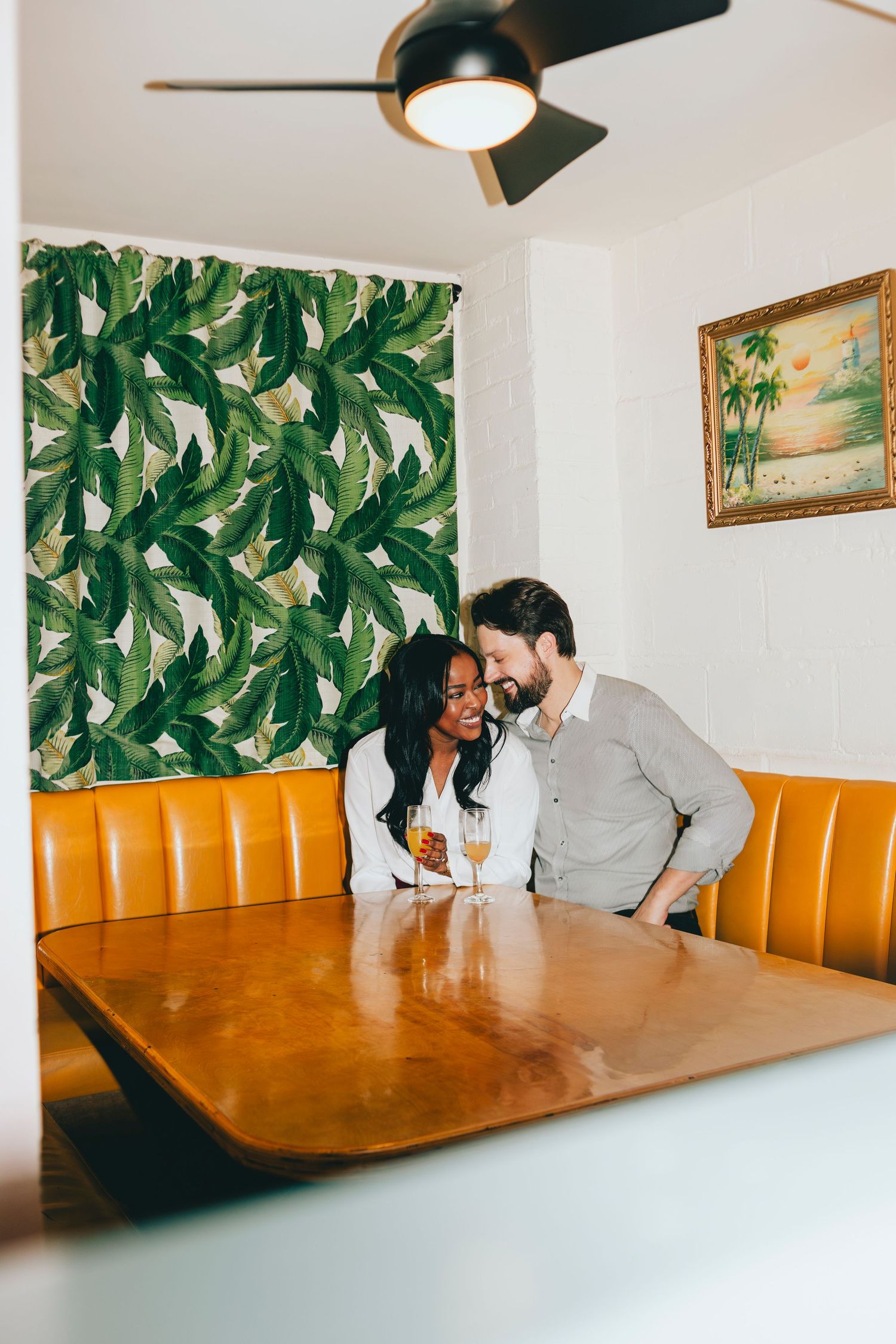 Restaurant interior with tropical leaf wallpaper and orange booth seating.
