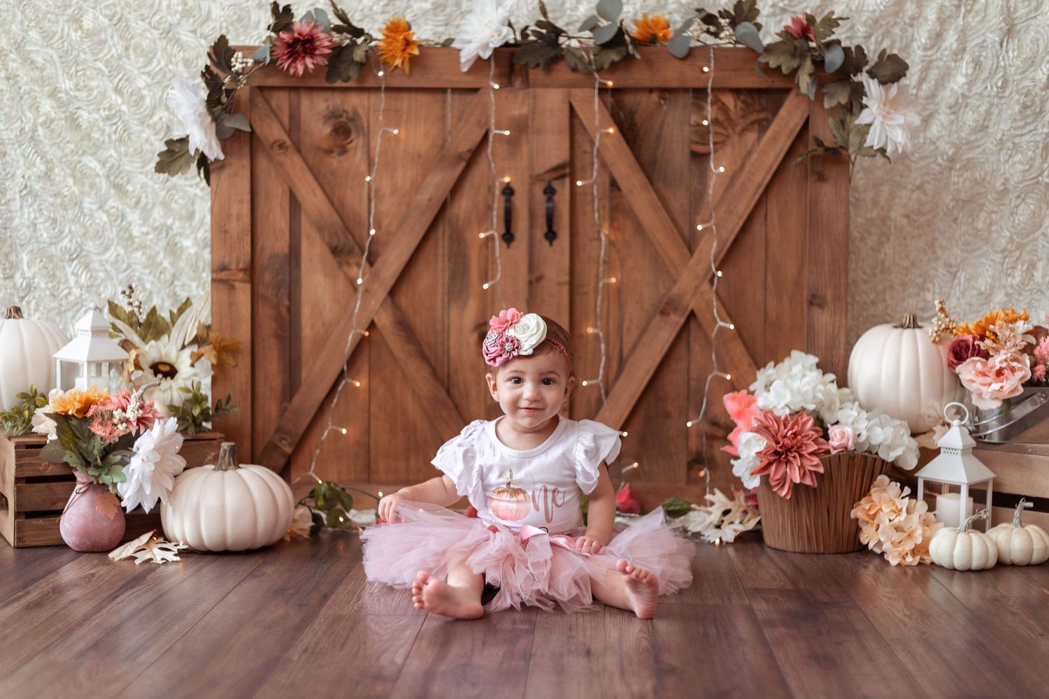 Fall themed baby photography setup with rustic barn doors, pink pumpkins, and autumn floral decorations.