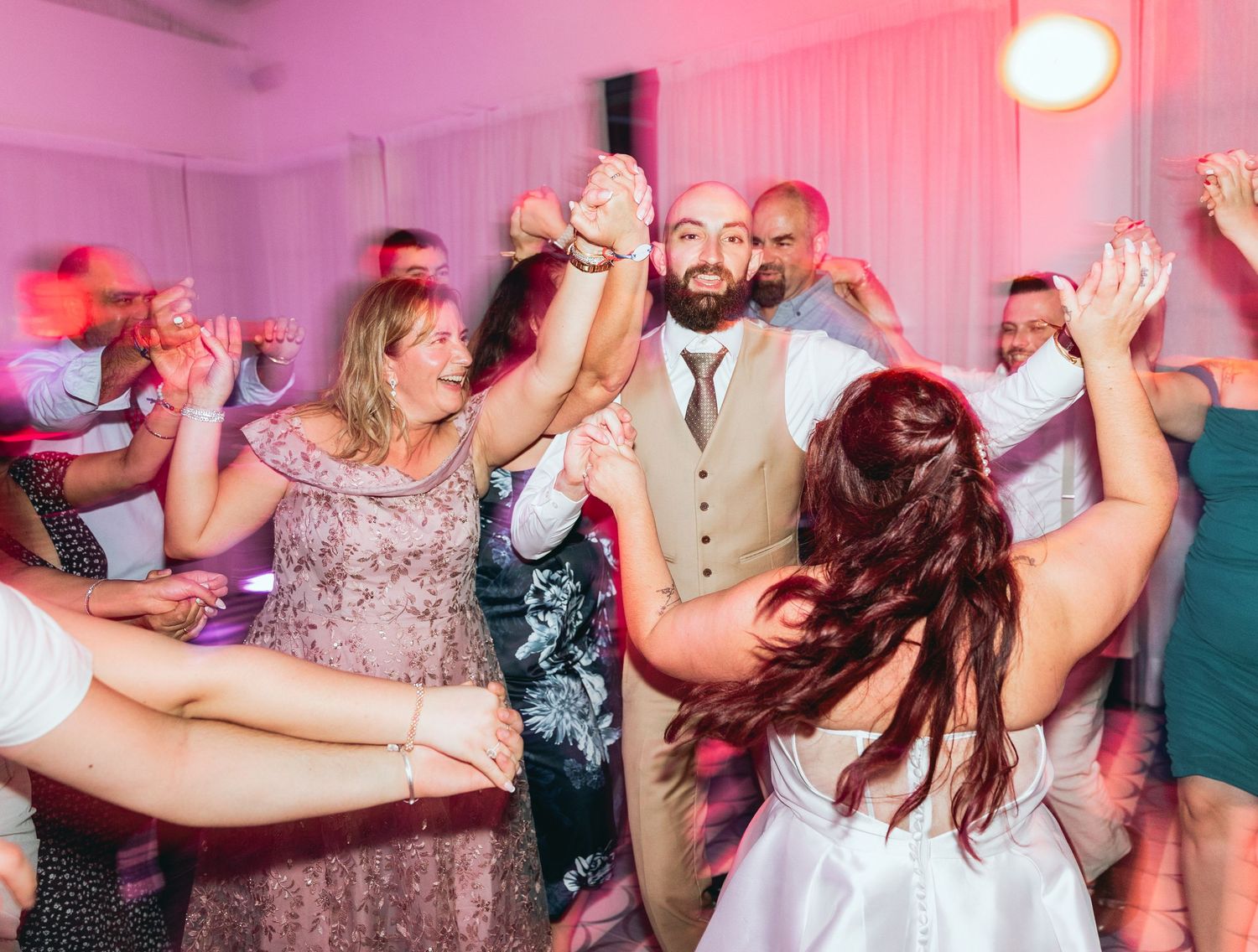Lively party scene with people dancing and celebrating under pink lighting.