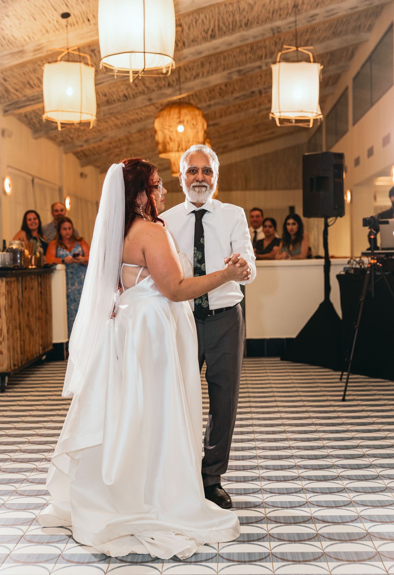 Wedding reception dance captured in rustic venue with geometric floor pattern.