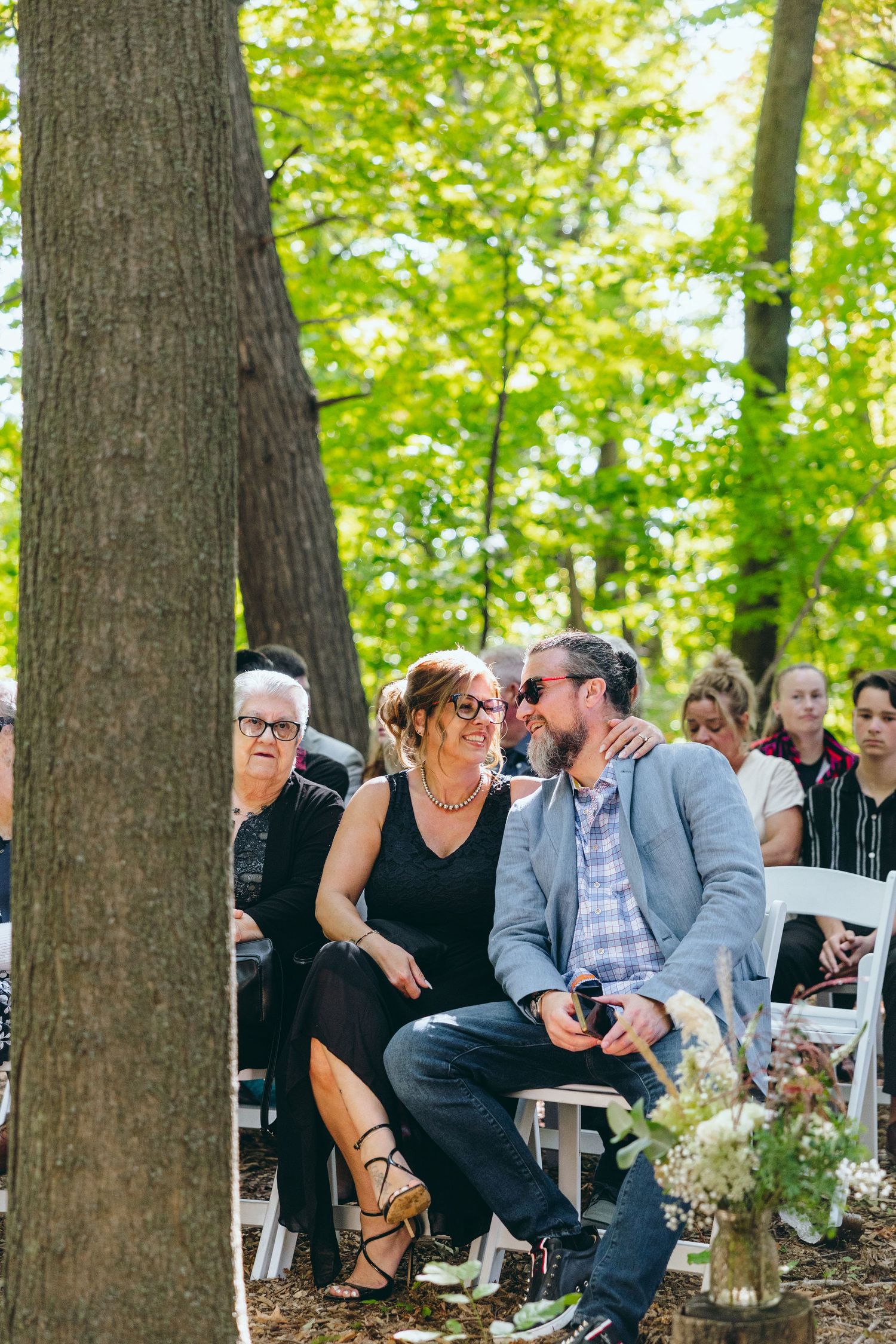 Wedding guests seated in wooden chairs enjoy the outdoor forest ceremony.