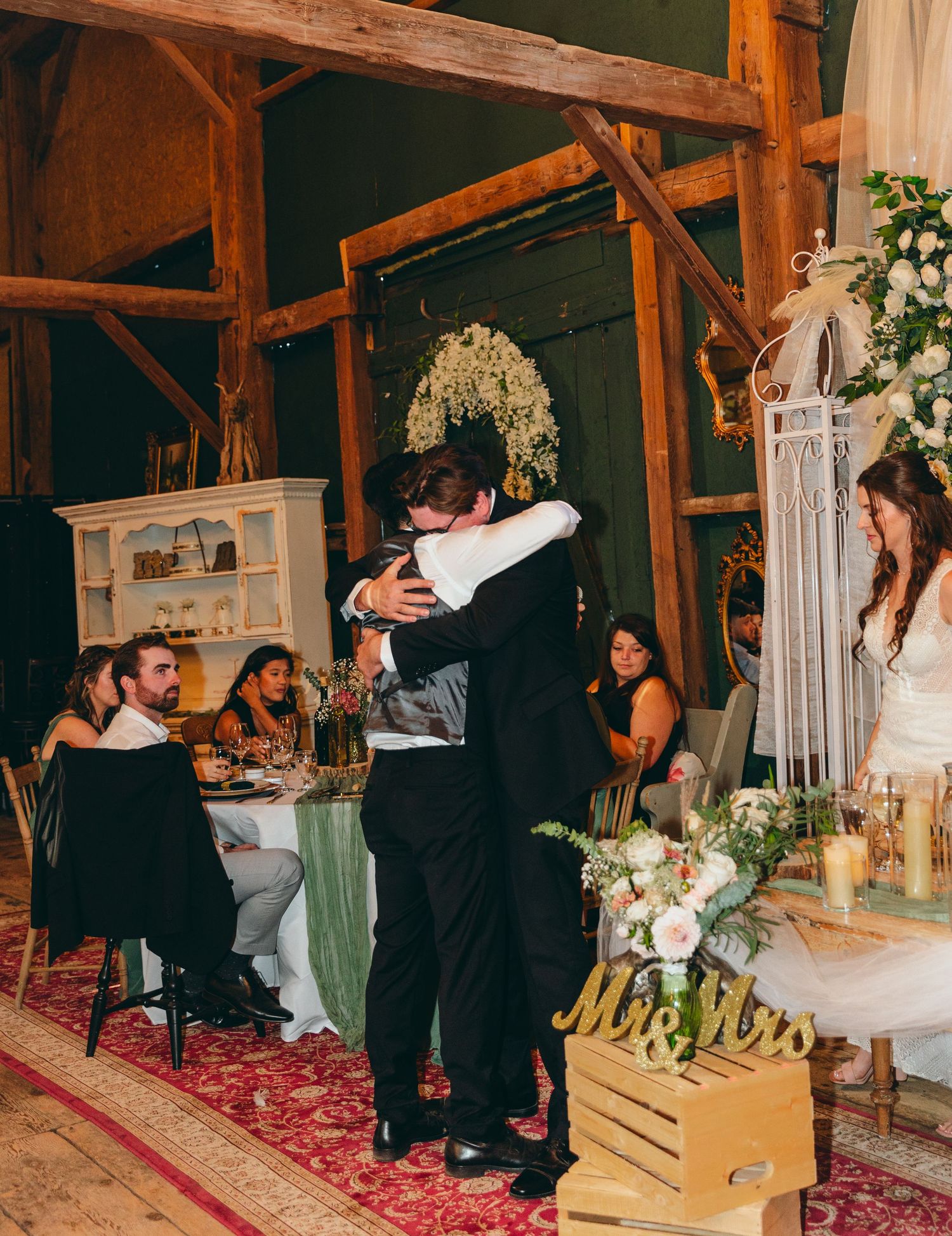 Wedding celebration in a rustic barn venue decorated with white drapes and floral arrangements.