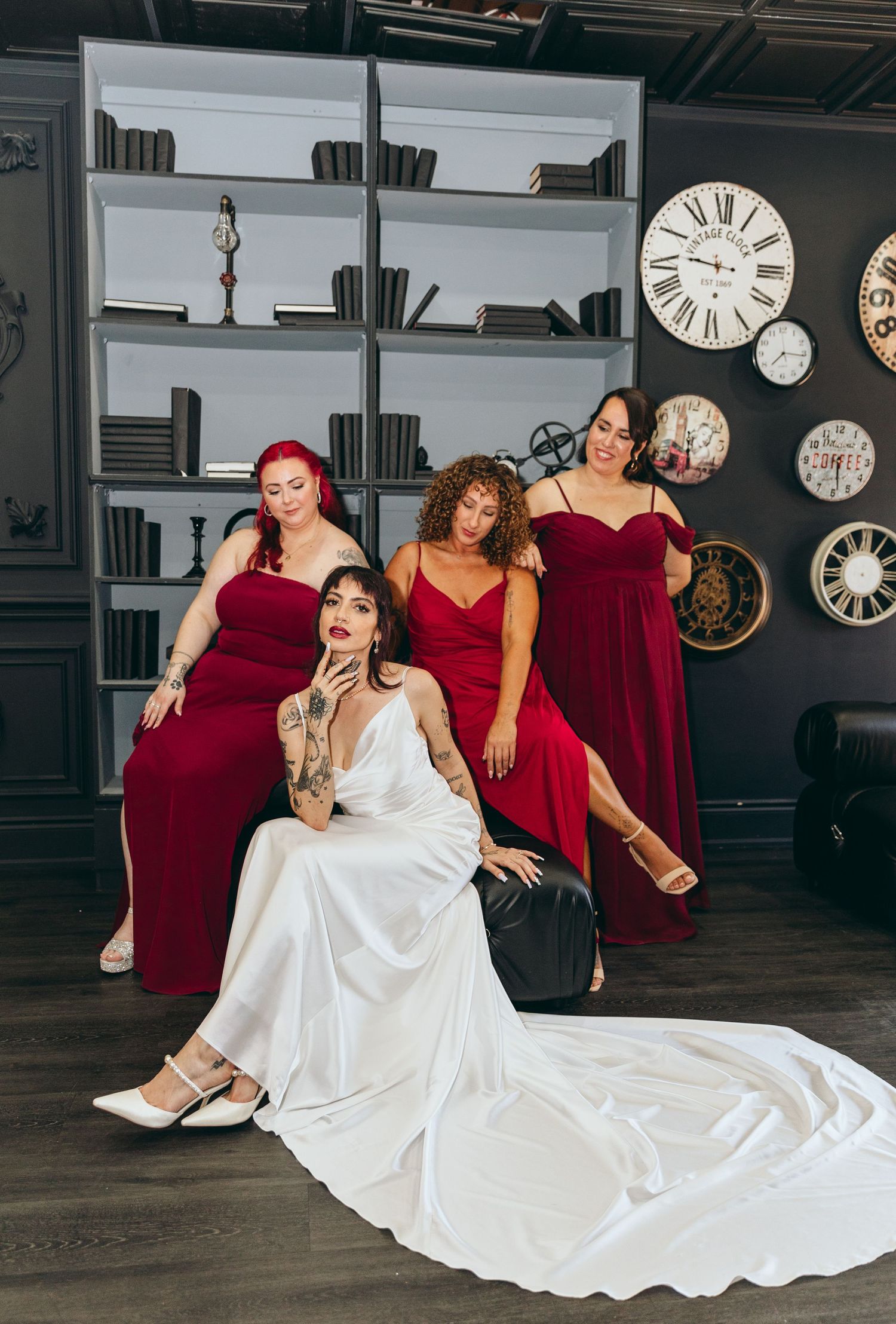 Bridal party in burgundy dresses posing with clocks and bookshelves in background.