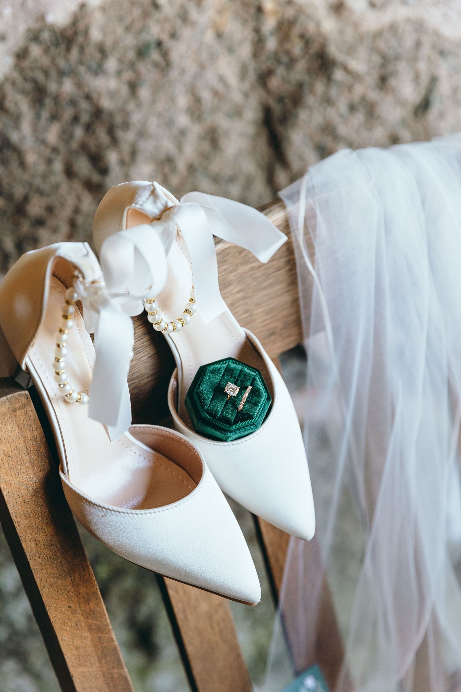 White wedding shoes and emerald green details arranged on wooden chairs.