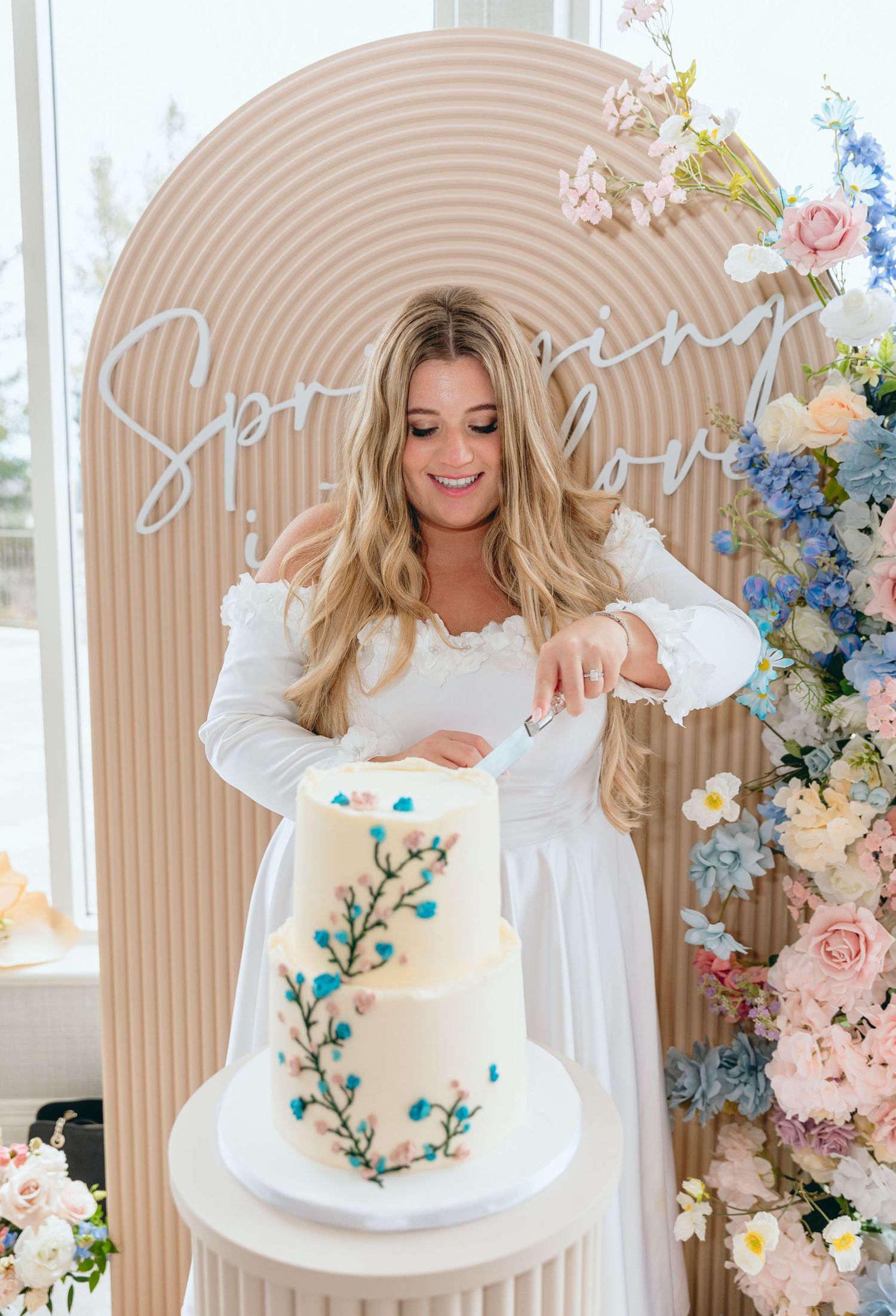 Beautiful white cake with delicate blue floral details displayed in front of a decorative arch.