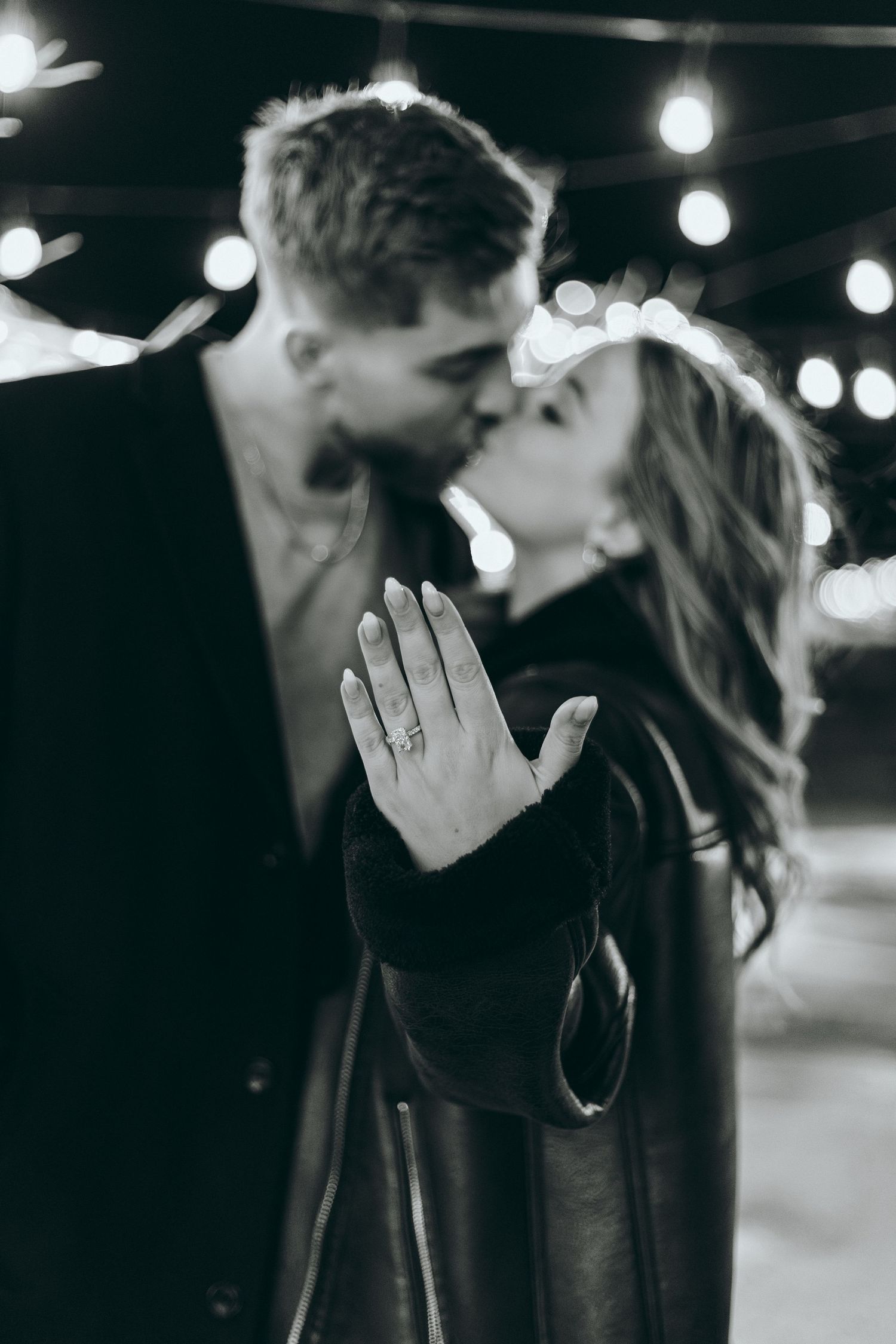 A black and white engagement photo showing a ring while a couple shares a romantic moment.