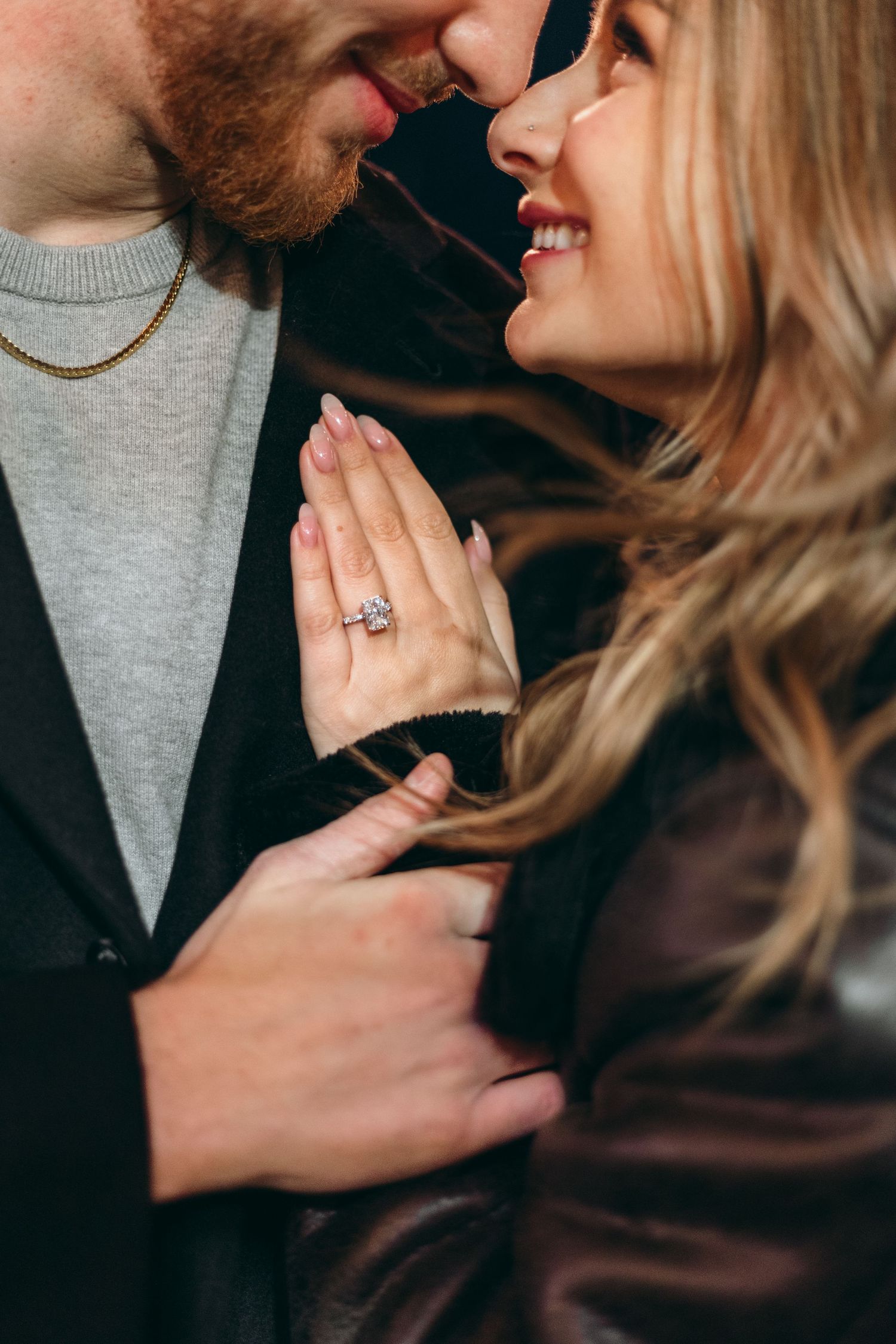 Close-up romantic engagement moment showing a couple embracing with a sparkling ring visible.