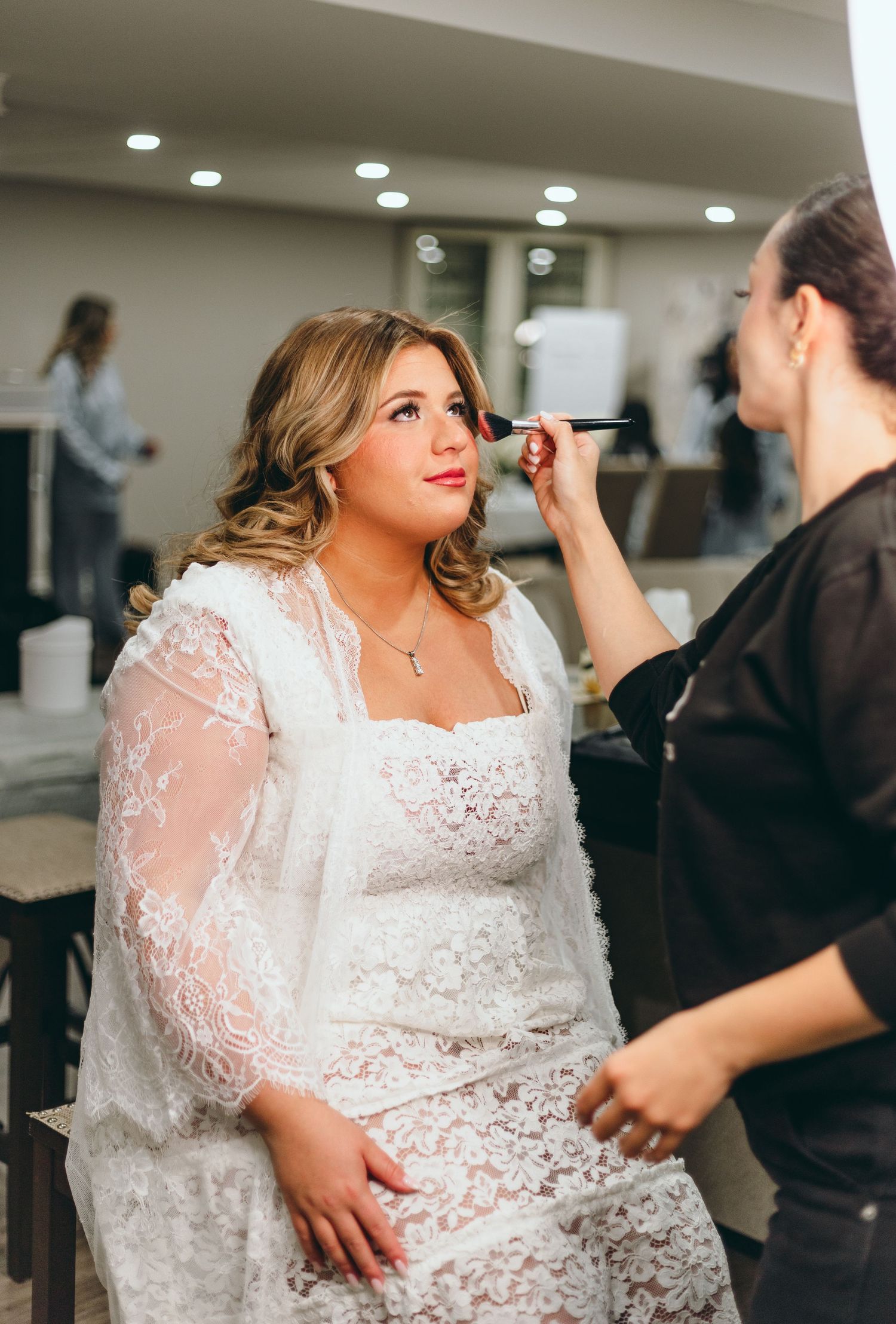 Bride in a beautiful lace wedding dress getting makeup done before the ceremony.