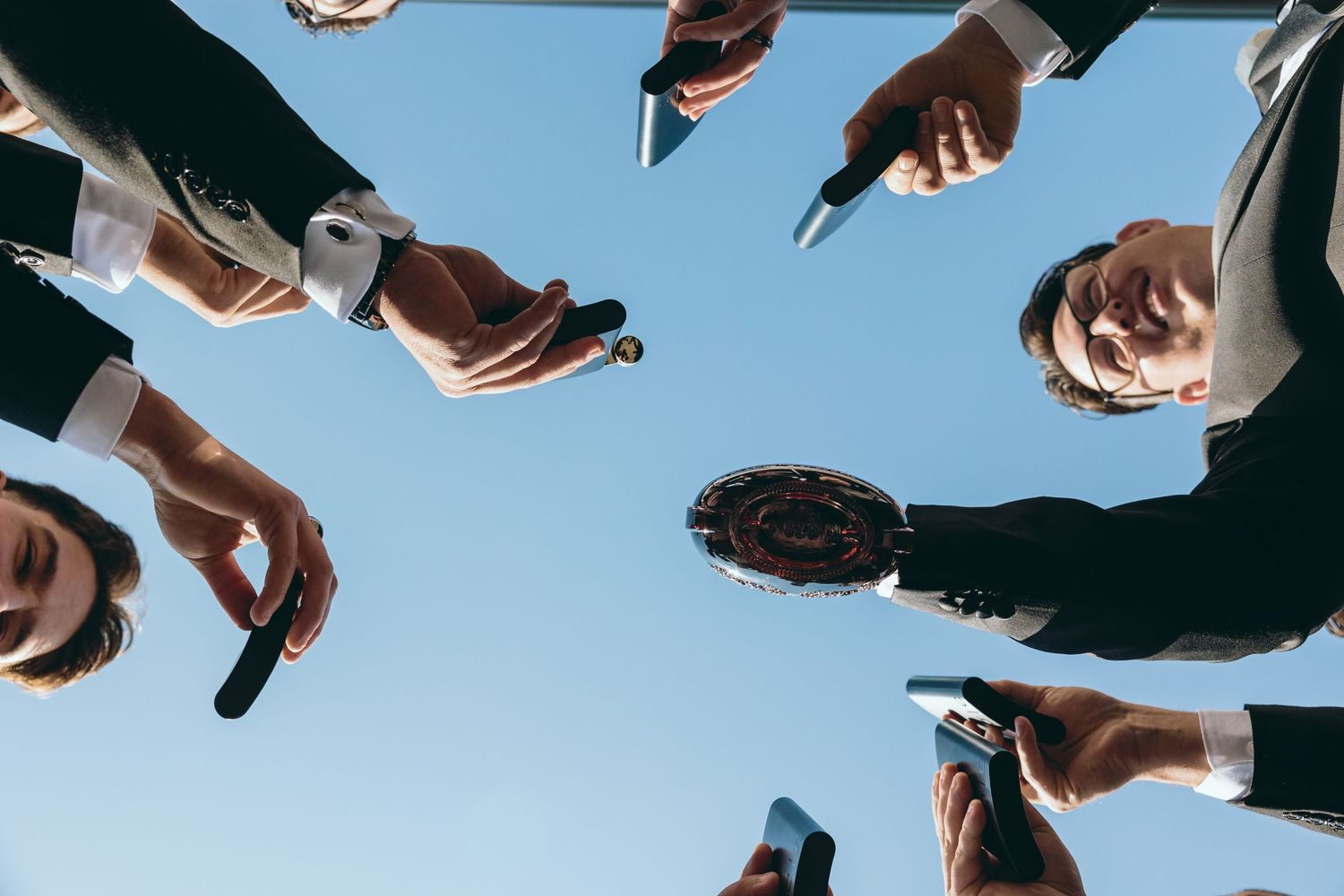 Low angle view of people holding phones in a circle against blue sky.