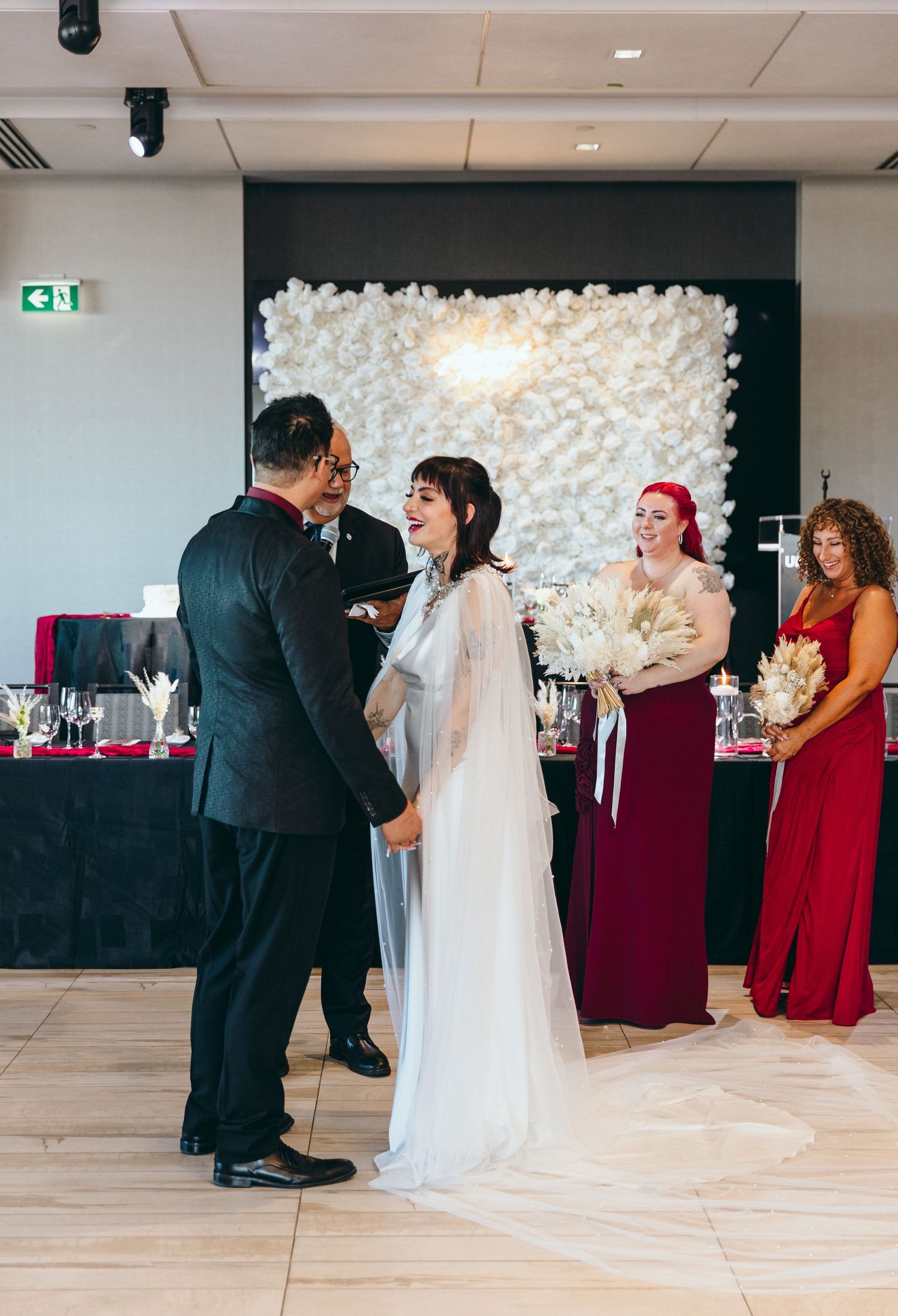 Wedding celebration in a modern venue with white floral backdrop and burgundy accents.