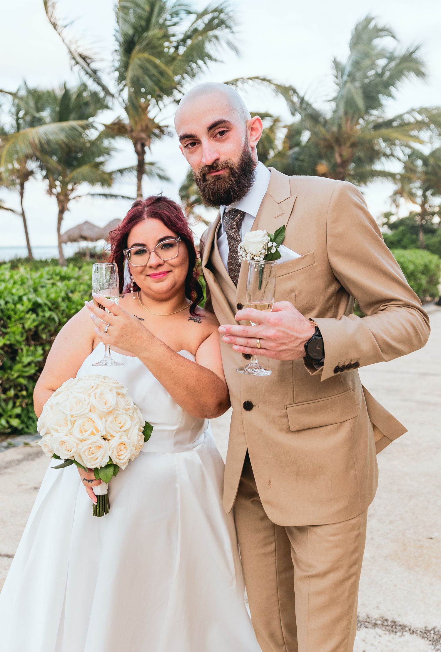 Newlyweds share intimate moments on a tropical beach in tan and white attire.