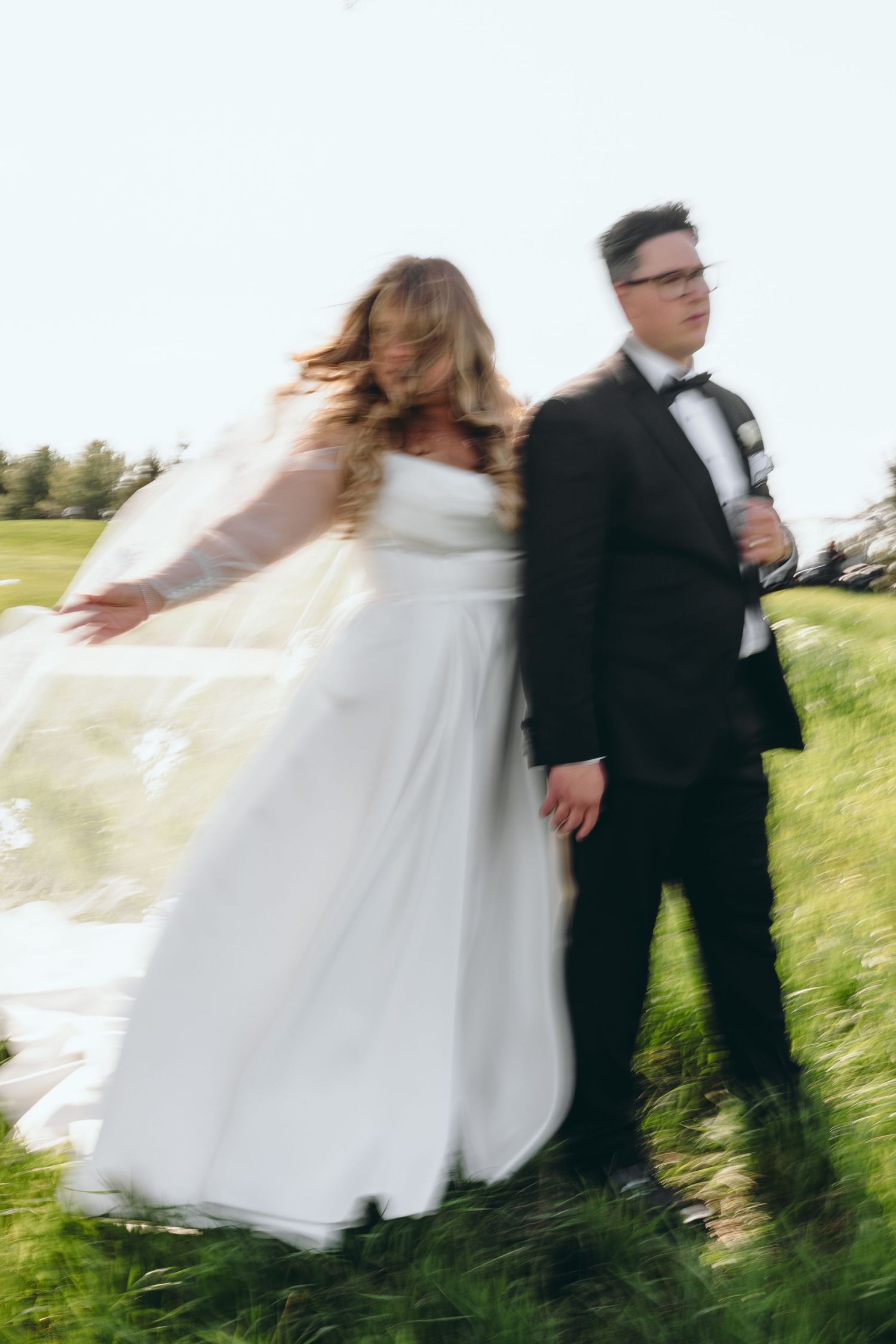 Motion-blur photograph of newlyweds in formal attire standing in a grassy field.