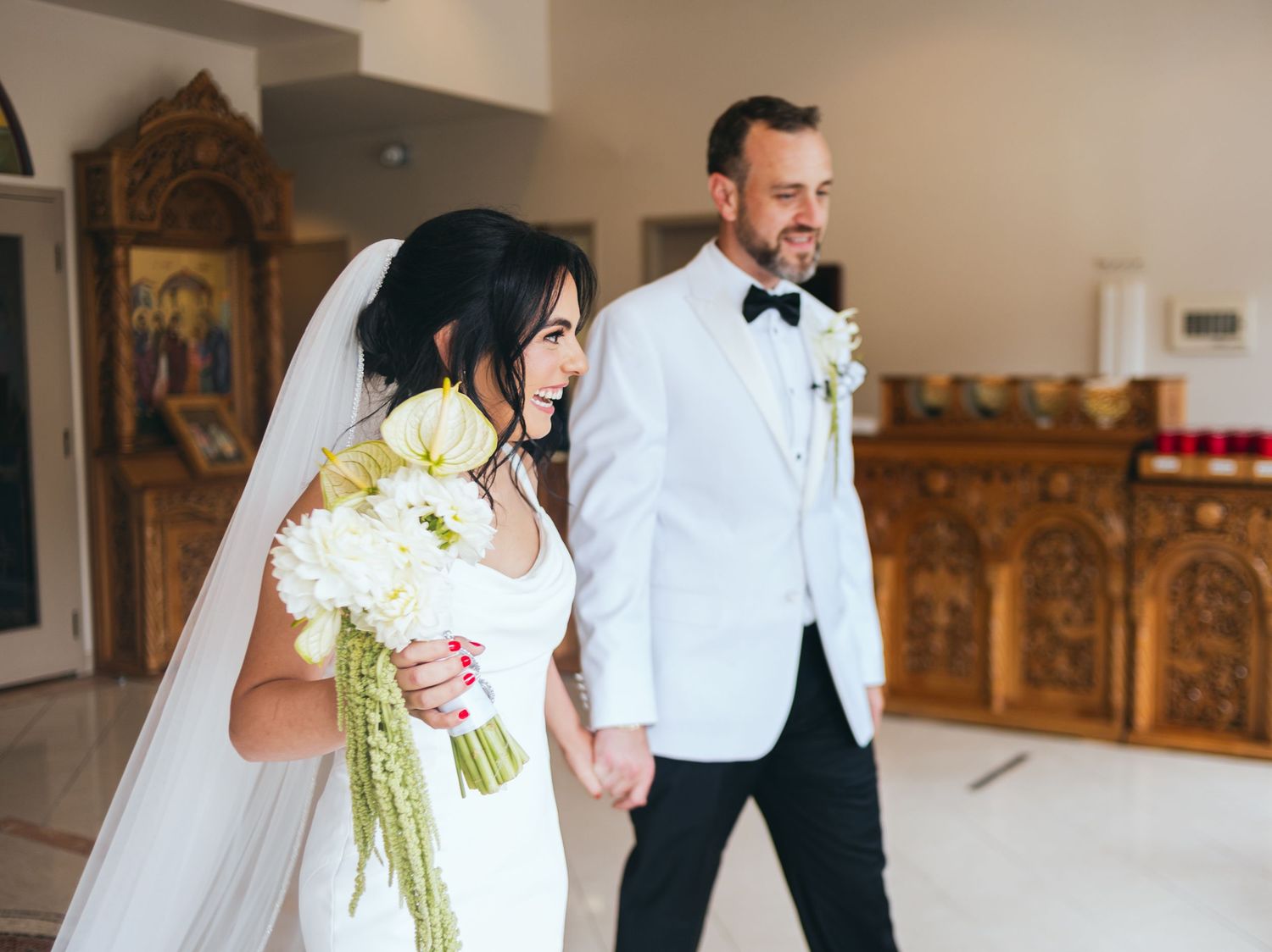 Wedding couple walks through elegant indoor venue with ornate gold decor.