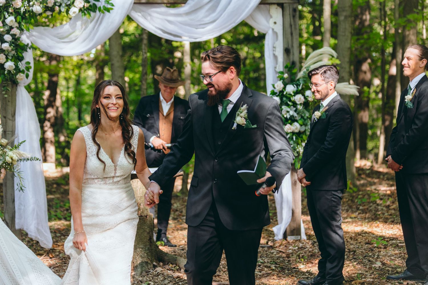 Outdoor wedding ceremony in a wooded area with white fabric draping between trees.