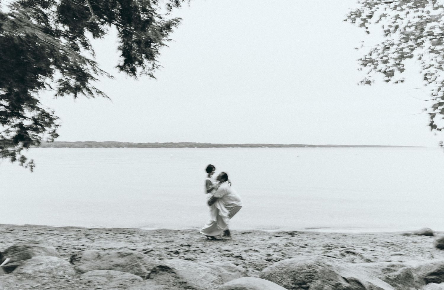 Black and white beach scene with couple embracing on rocky shore.