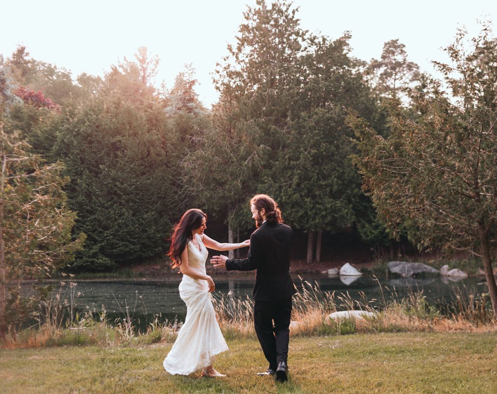 A couple in wedding attire dances playfully in a garden setting at sunset.