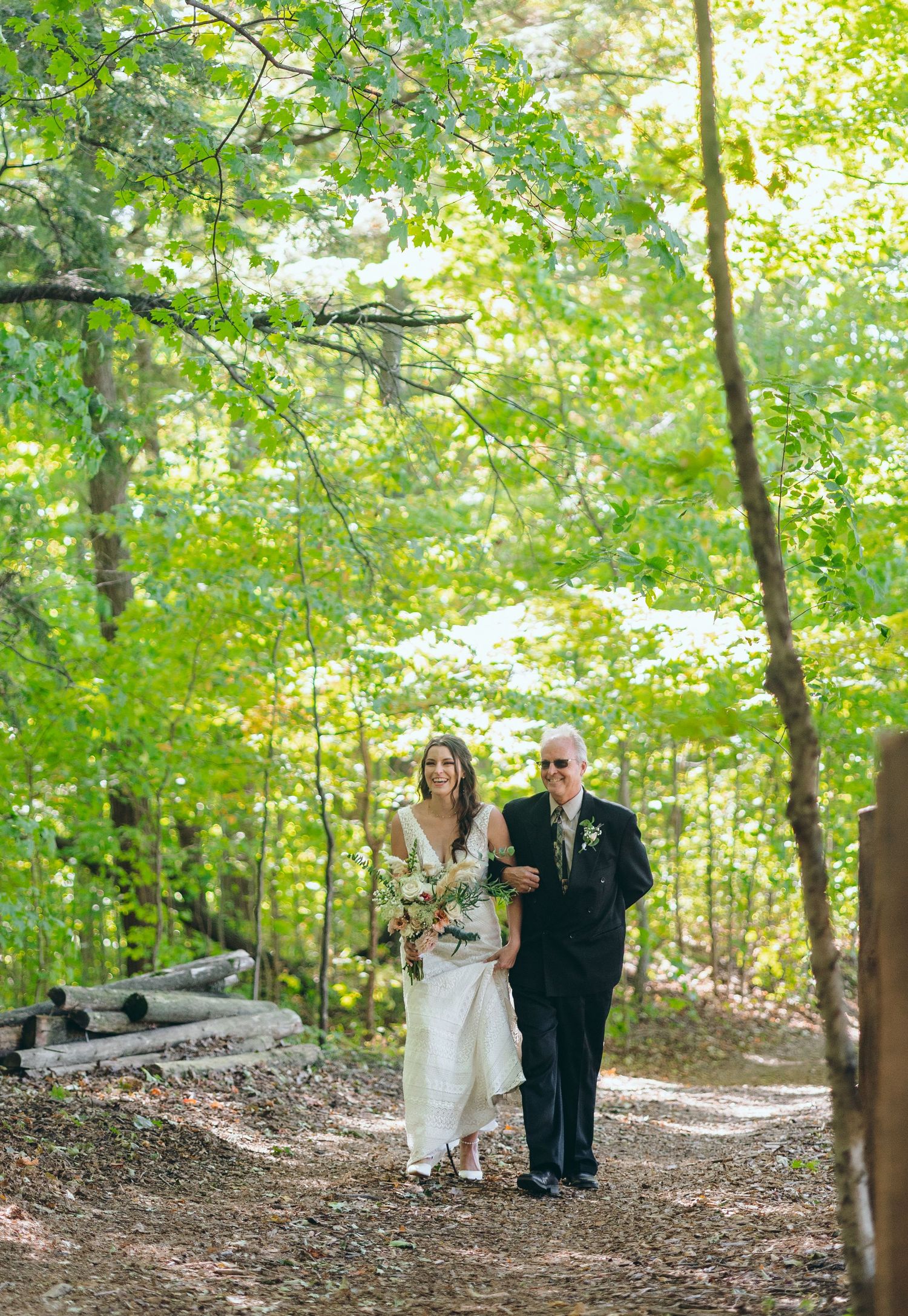 Wedding party walking through a sunlit forest path during an outdoor ceremony.