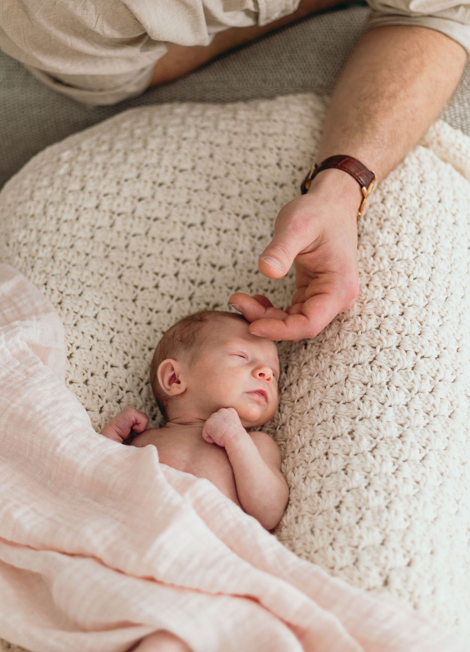 Gentle lifestyle newborn session on textured cream blanket with soft pink accents.