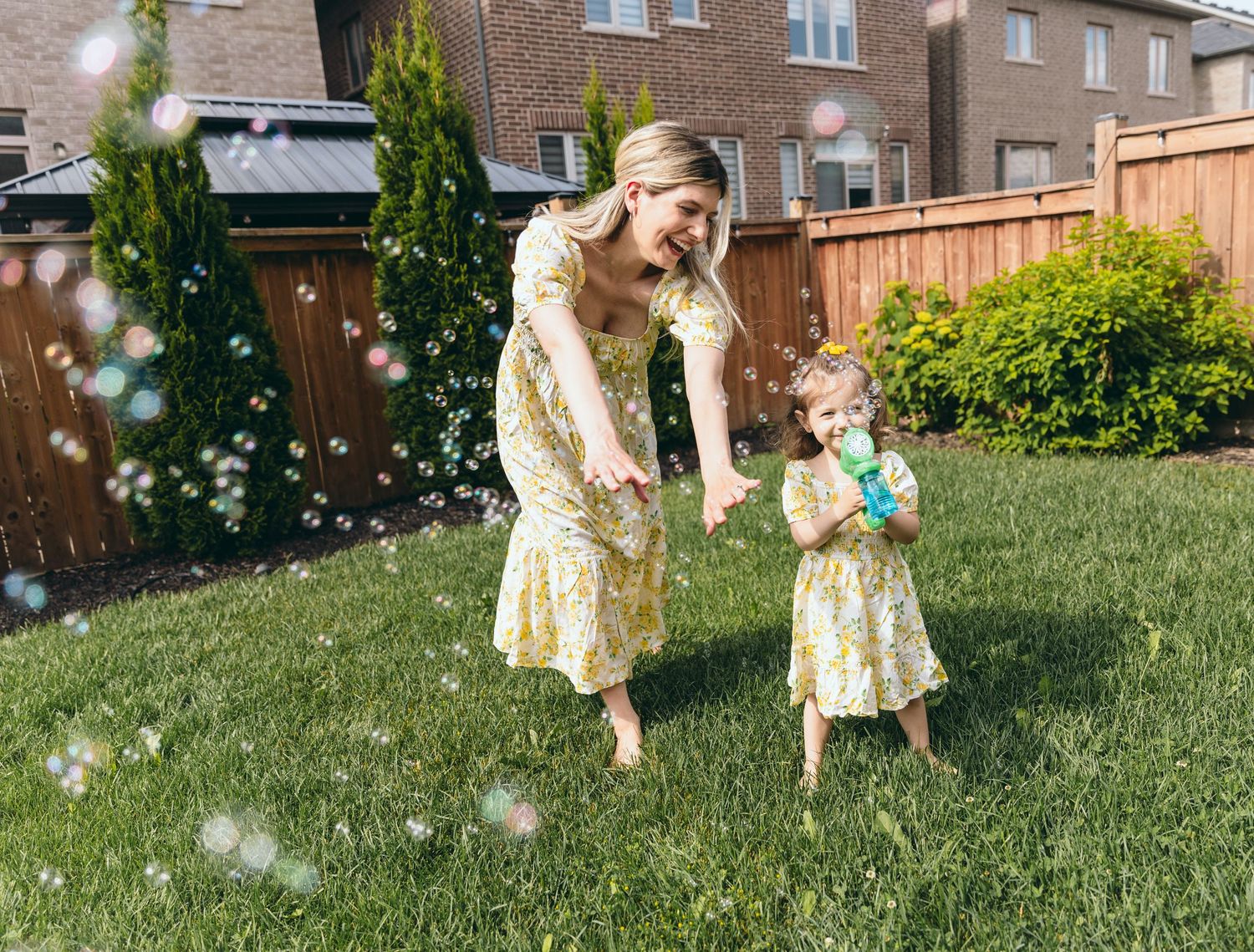 Playful scene in a backyard with yellow dresses and bubbles floating through the air.