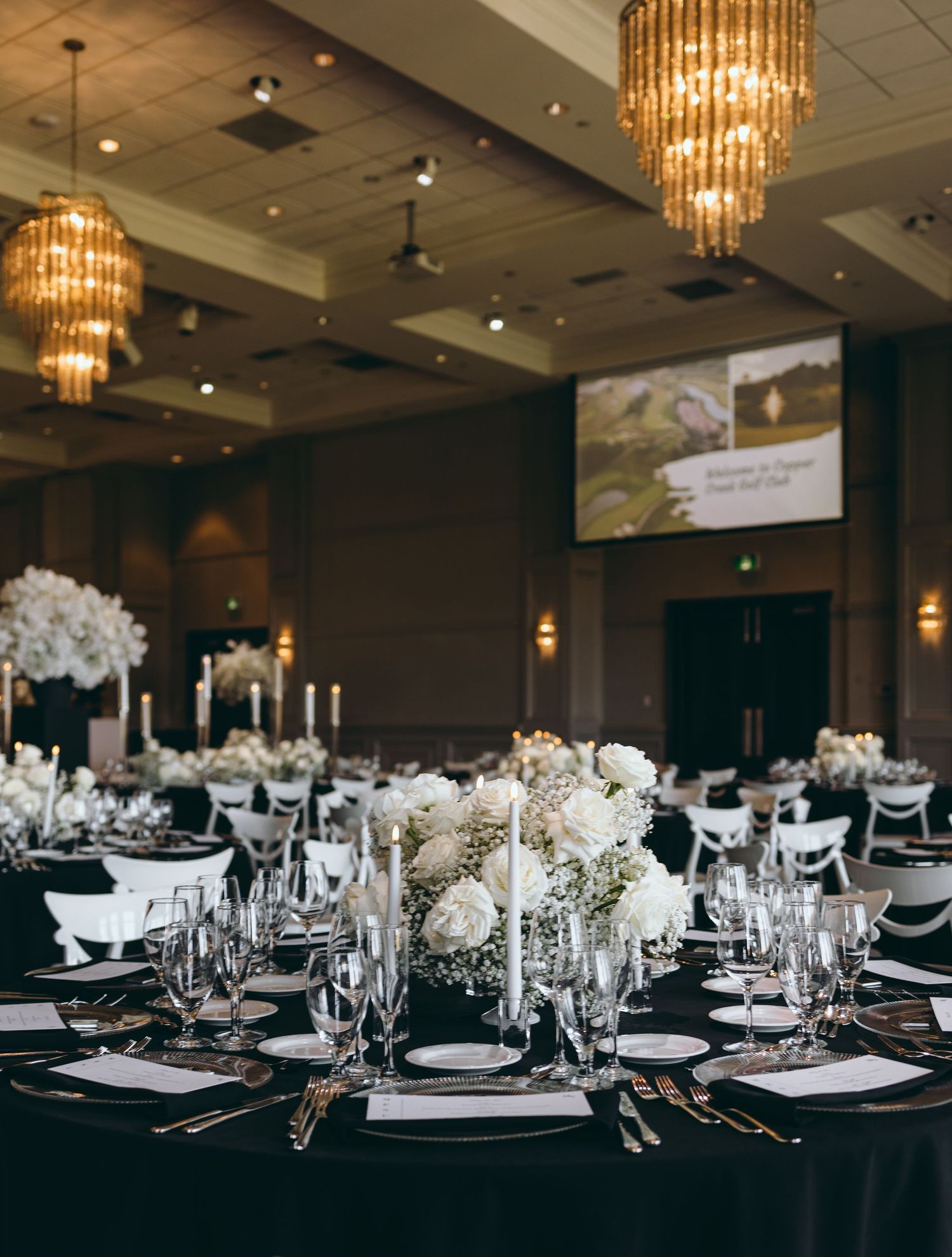 Formal wedding reception table settings with white floral centerpieces and crystal chandeliers.