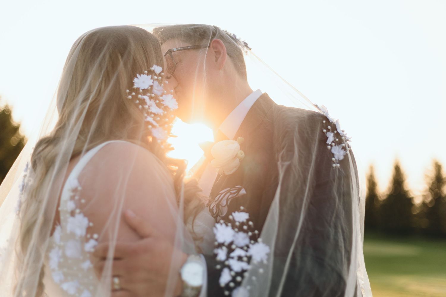 Sunlight streams through a wedding veil as a couple shares an intimate moment outdoors.