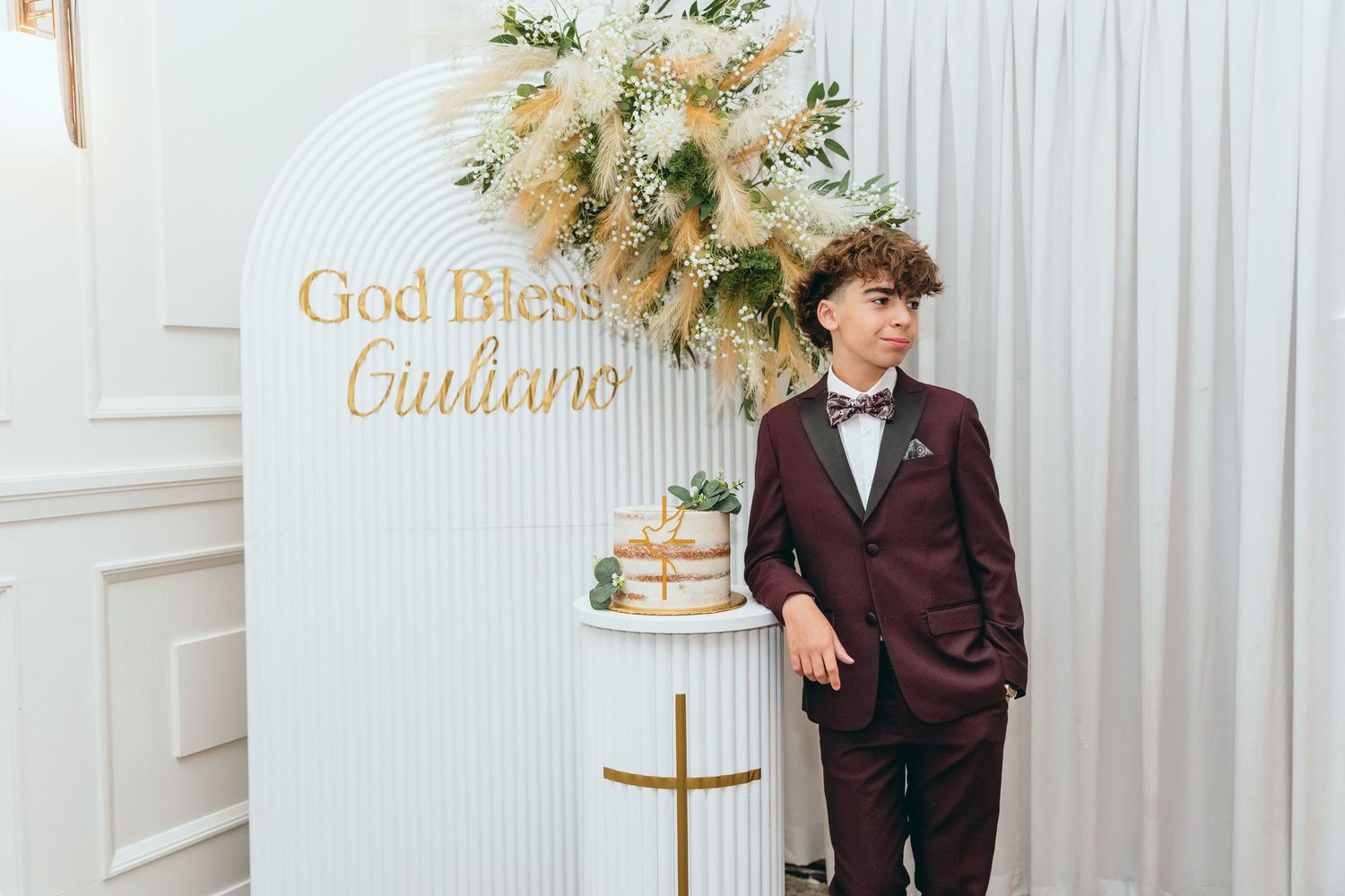 A formal event setup featuring an elegant arch with 'God Bless Guiliana' text and floral decorations.