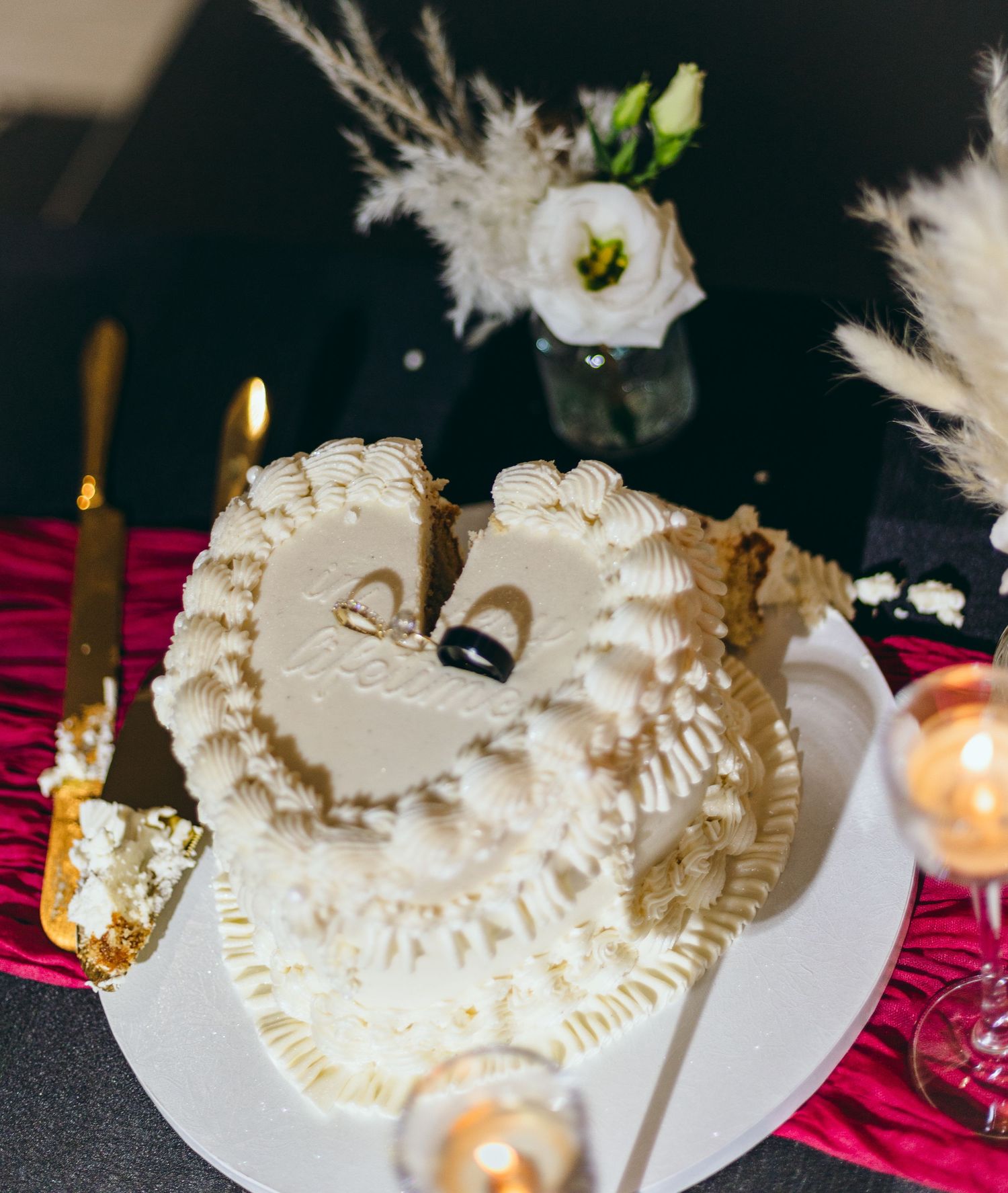 An elegant white wedding cake displayed with candlelight on a red tablecloth.