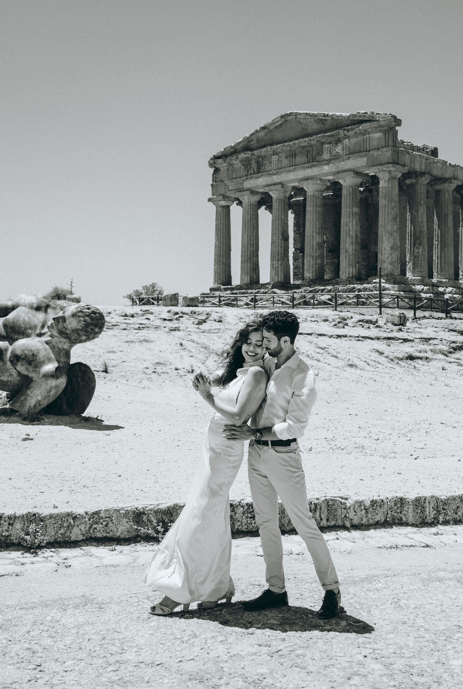 A romantic couple dances and poses near ancient Greek temple columns in black and white.
