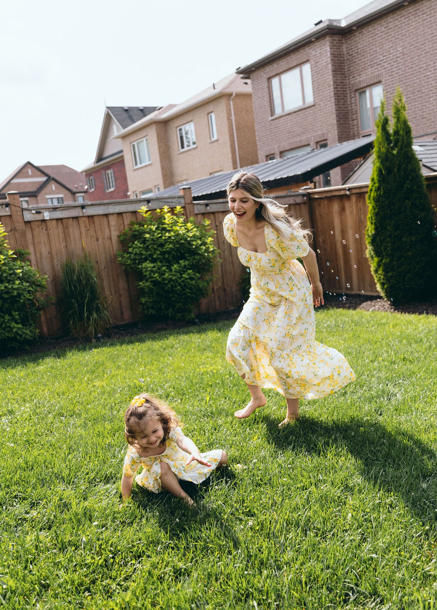 Dancing and twirling in yellow floral dresses on a sunlit lawn.