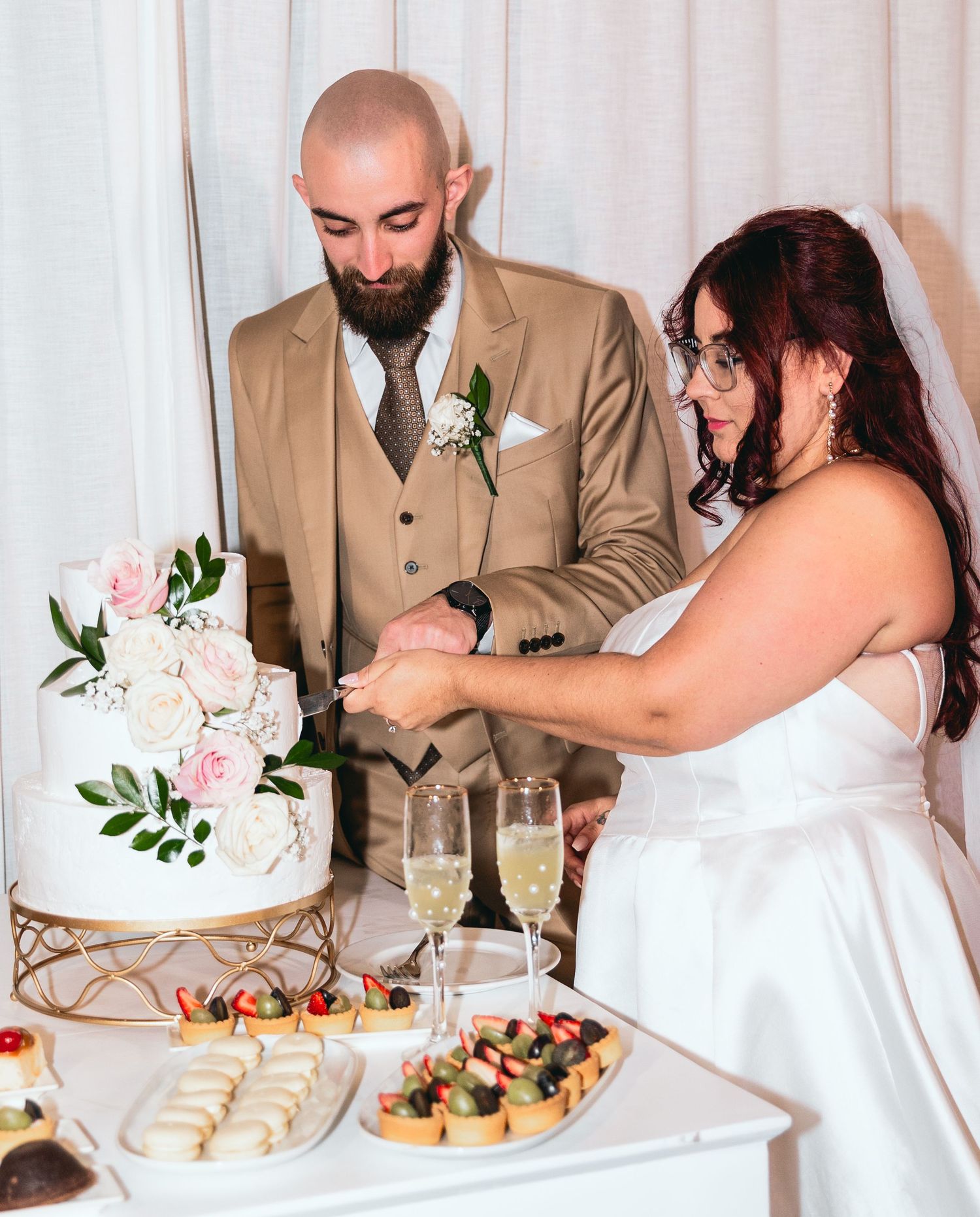 A couple cuts their elegant white wedding cake decorated with pink roses.